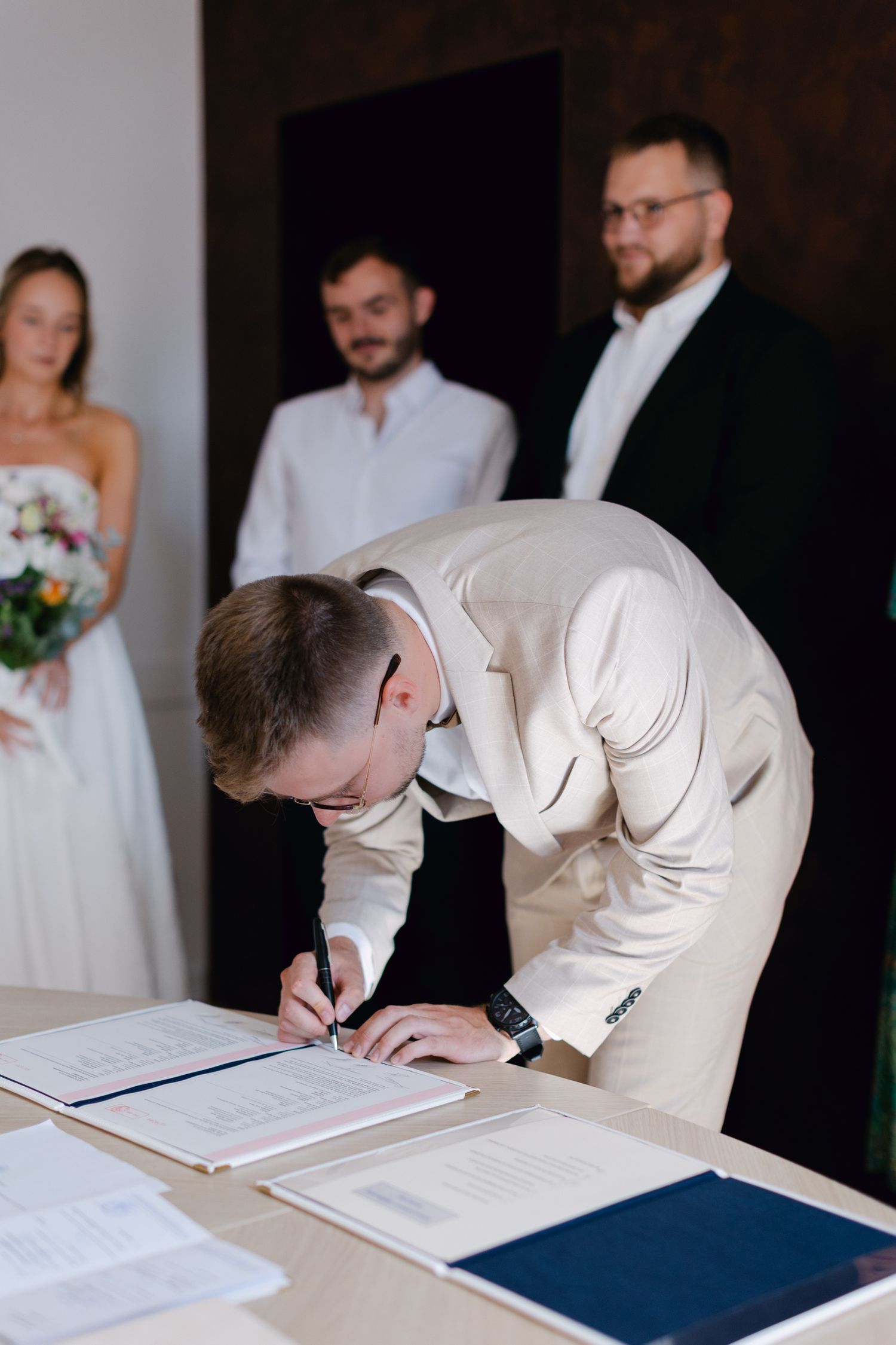 Marié en costume crème signant des documents officiels de mariage à la table d'enregistrement de la cérémonie de mariage.