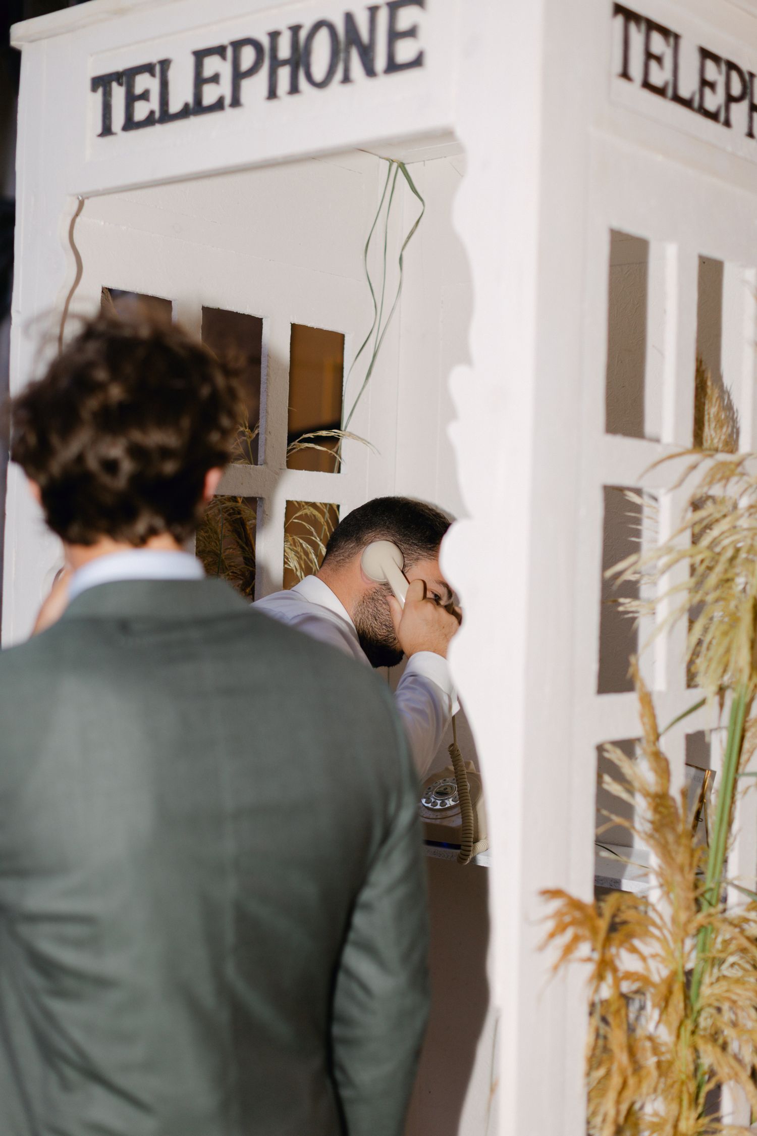 Invité de mariage utilisant un accessoire de cabine téléphonique blanc vintage dans un élégant lieu de réception de mariage.