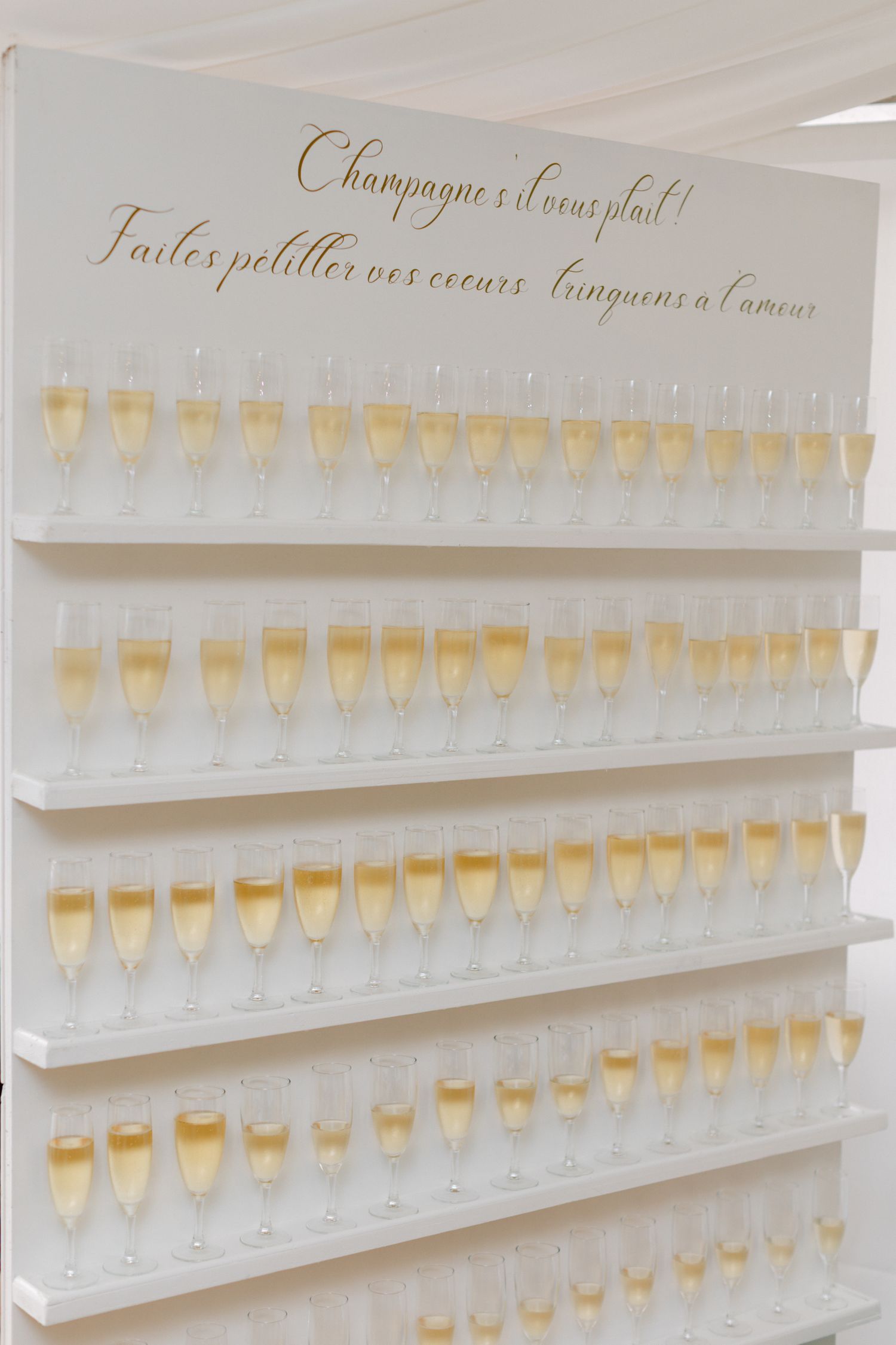 Élégant présentoir mural de champagne avec des rangées de flûtes remplies et une signalisation de calligraphie française.