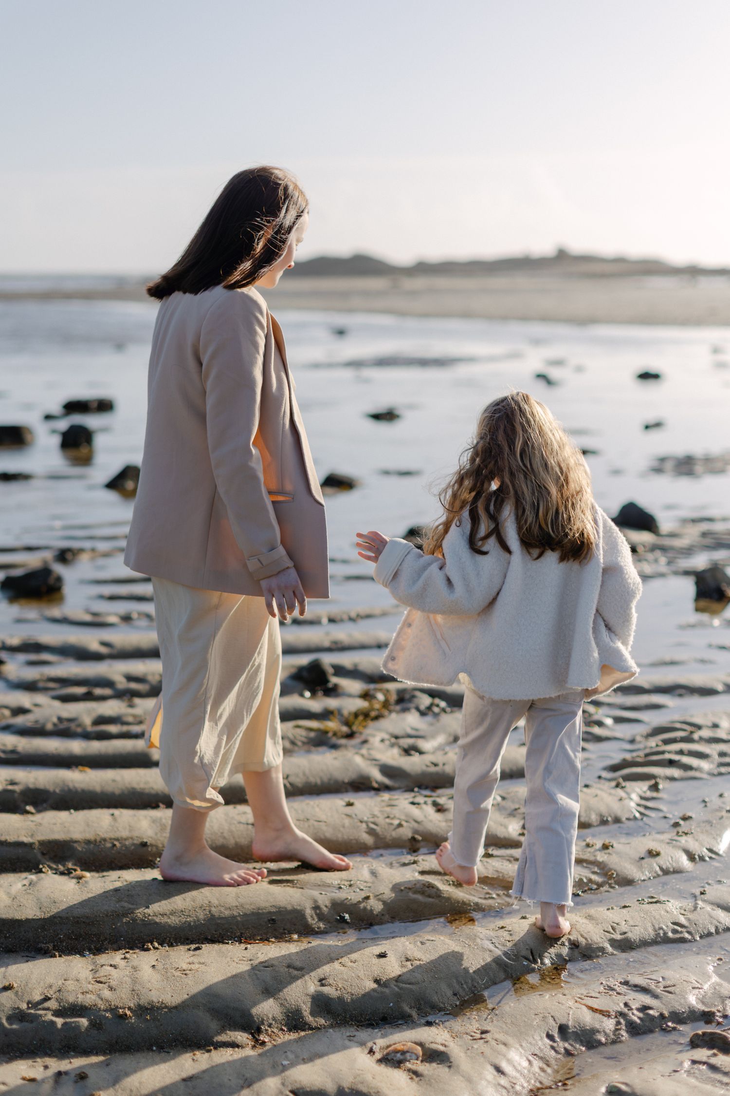 Une mère et sa jeune fille marchent pieds nus ensemble le long d'une plage de sable au coucher du soleil.