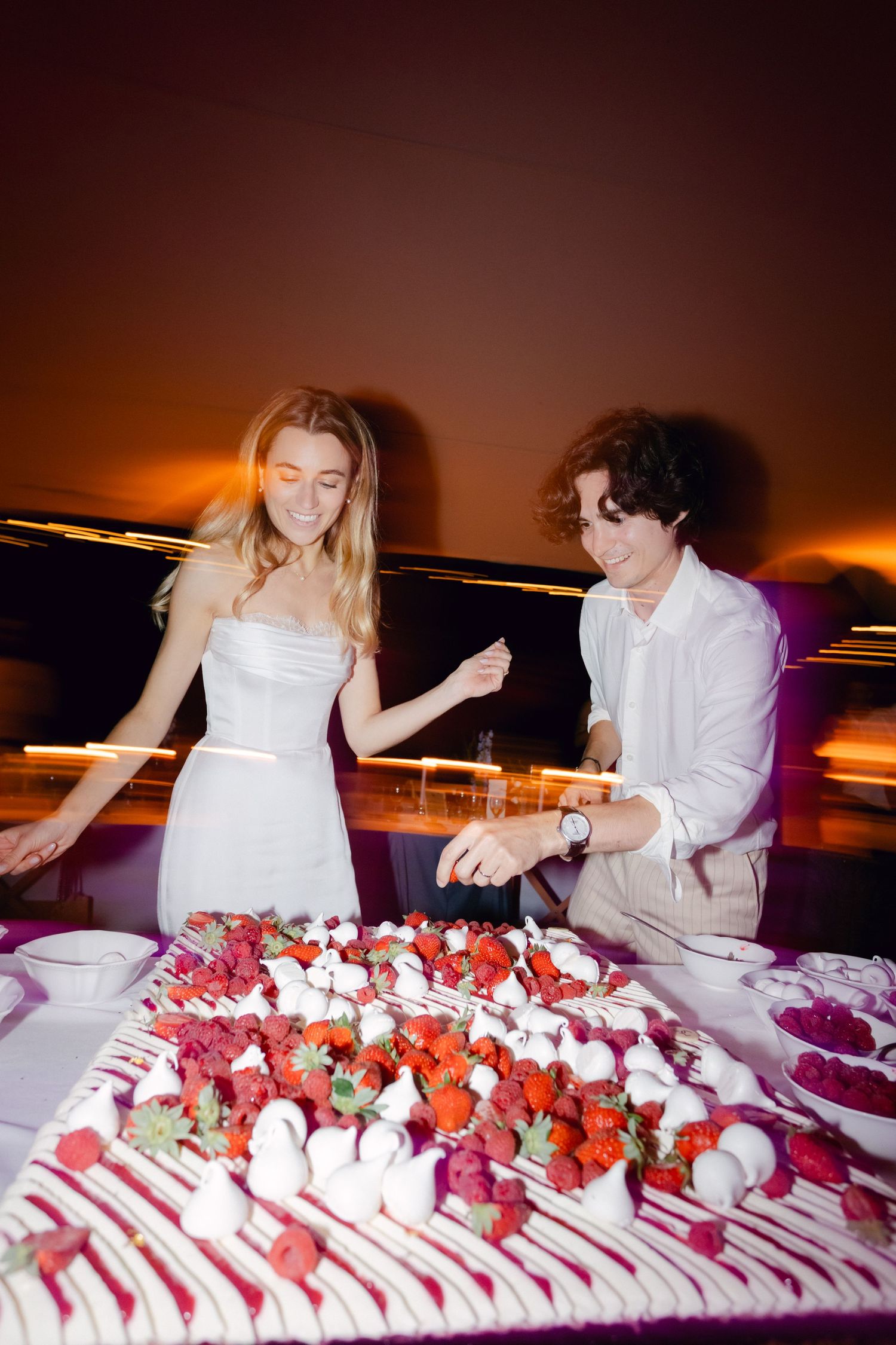 La mariée et le marié coupent ensemble un gâteau de mariage à la fraise et à la crème lors de la réception du soir.