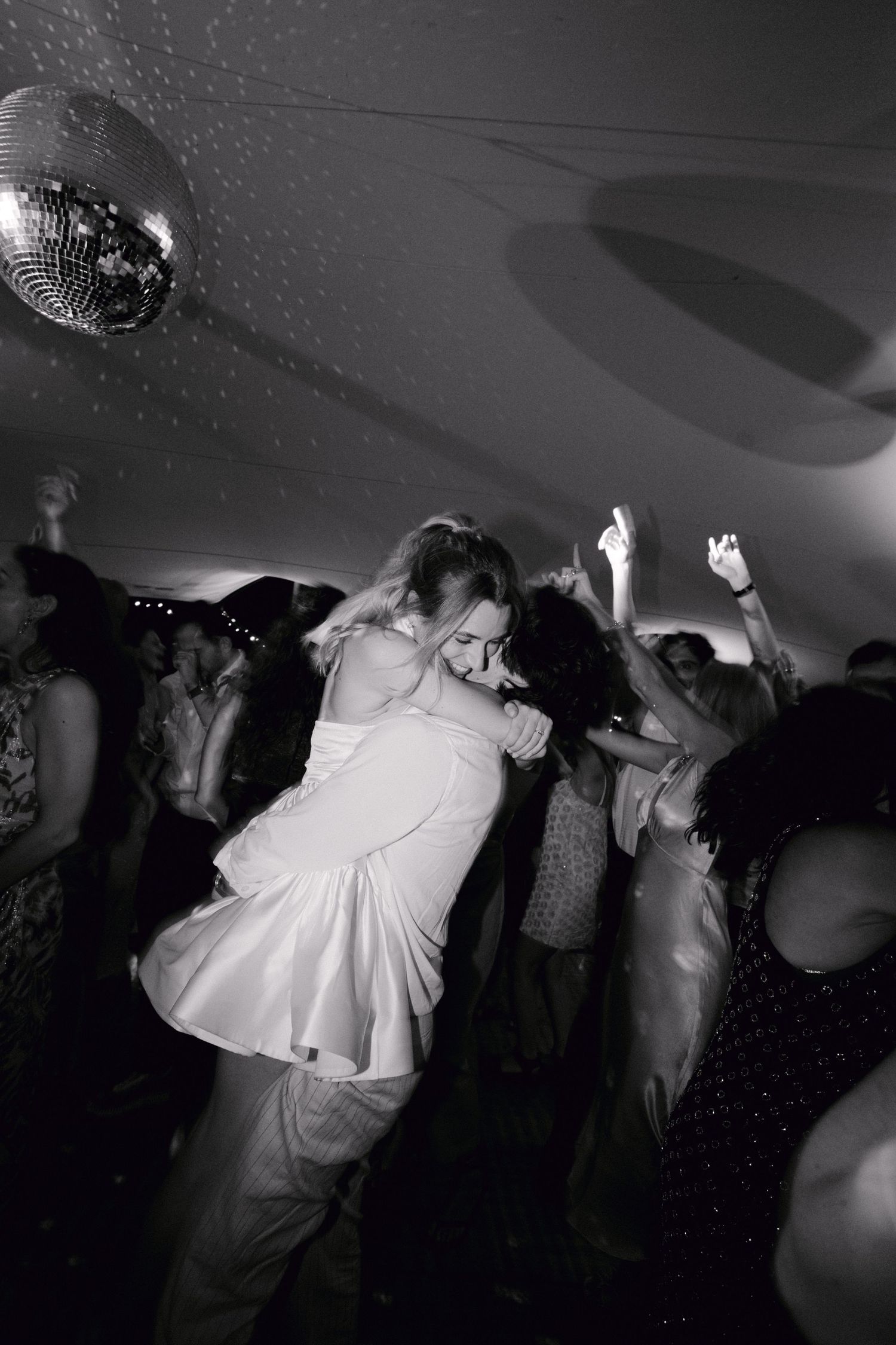 Photo en noir et blanc de la mariée soulevée par le marié sur une piste de danse de mariage bondée.