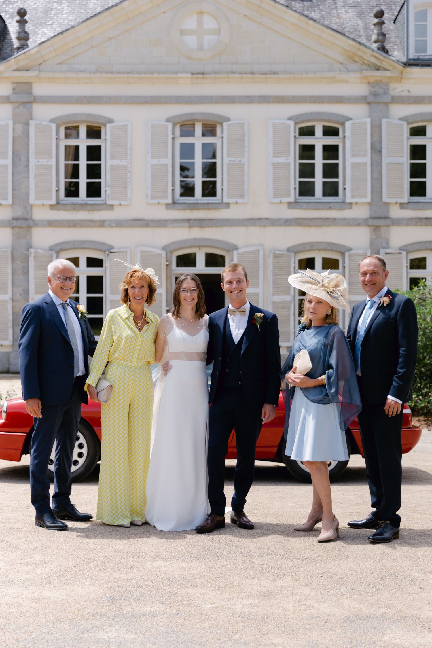 Fête de mariage de six personnes posant devant un château français, mariée en robe blanche avec le marié et les membres de la famille.