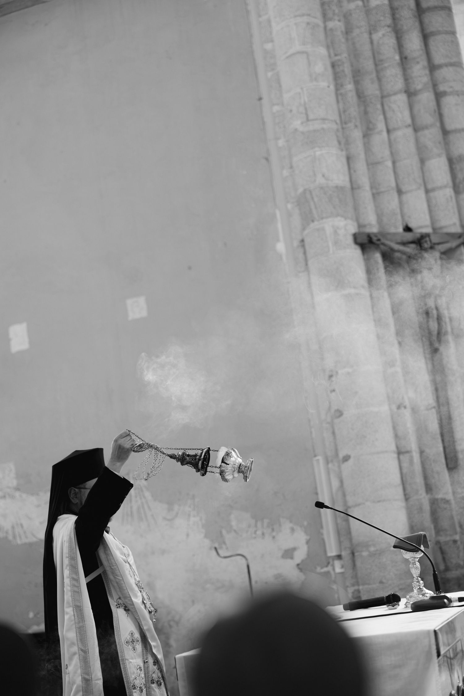 Black and white photo of a priest swinging a thurible with incense smoke rising during a church ceremony.