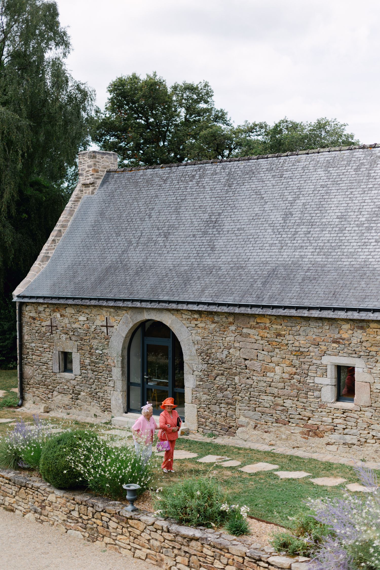 Deux invités marchant à l'extérieur d'un charmant lieu de mariage en pierre rustique entouré de jardins.