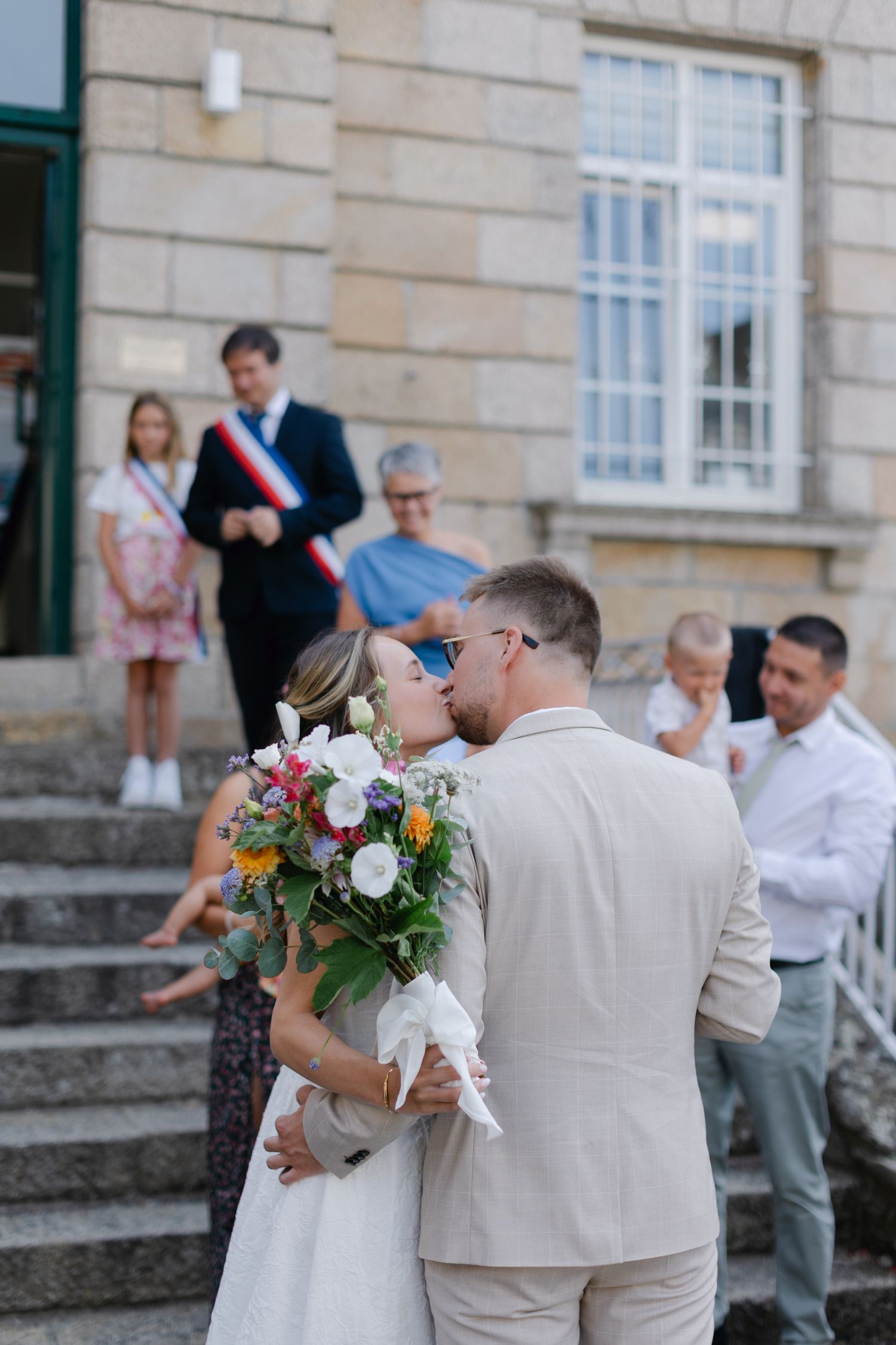 Les jeunes mariés partagent le premier baiser sur les marches à l'extérieur du French Hotel de Ville alors que l'officier et les invités reg