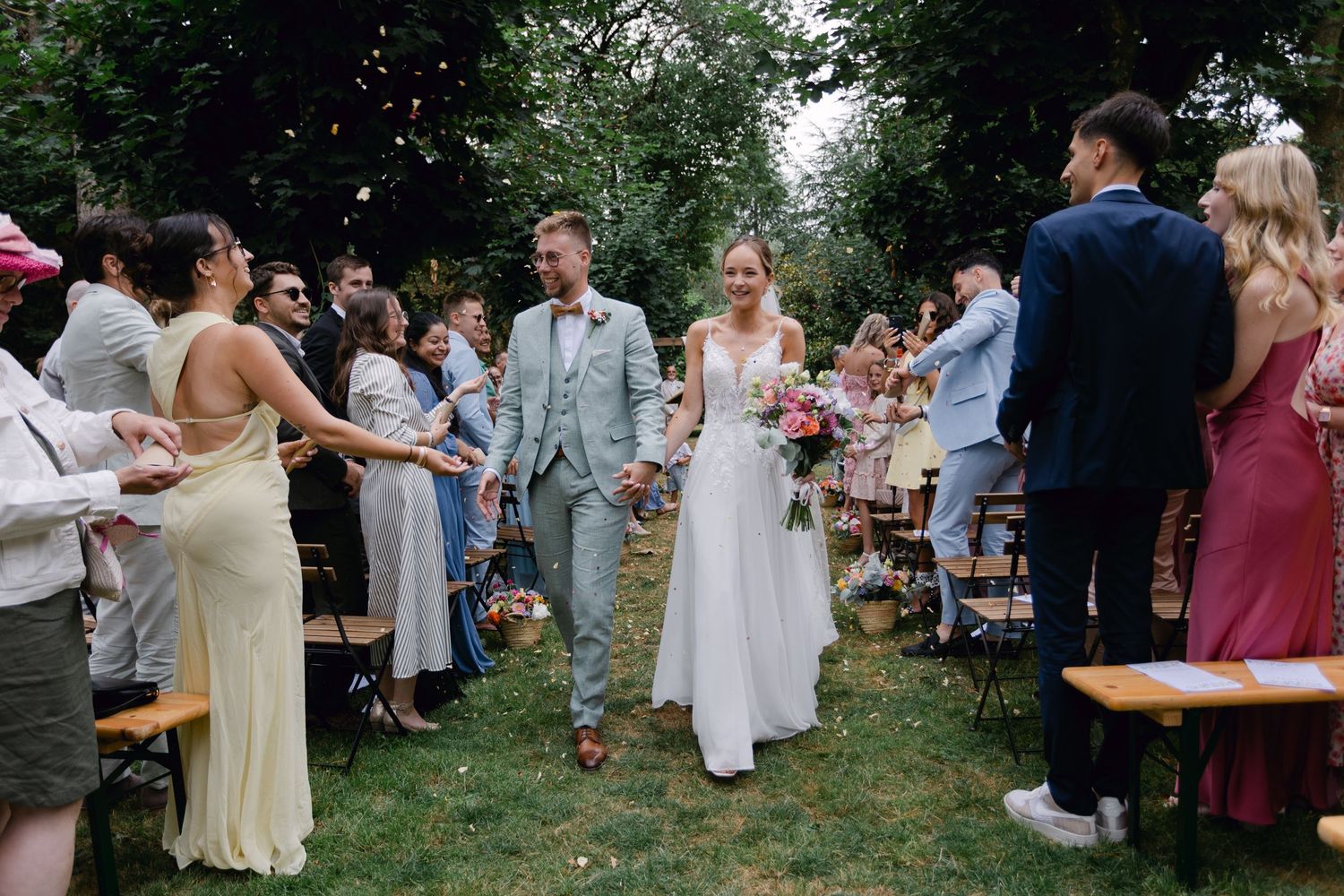 Couple de jeunes mariés marchant dans l'allée alors que les invités les assondent de confettis lors d'un mariage dans le jardin en plein air