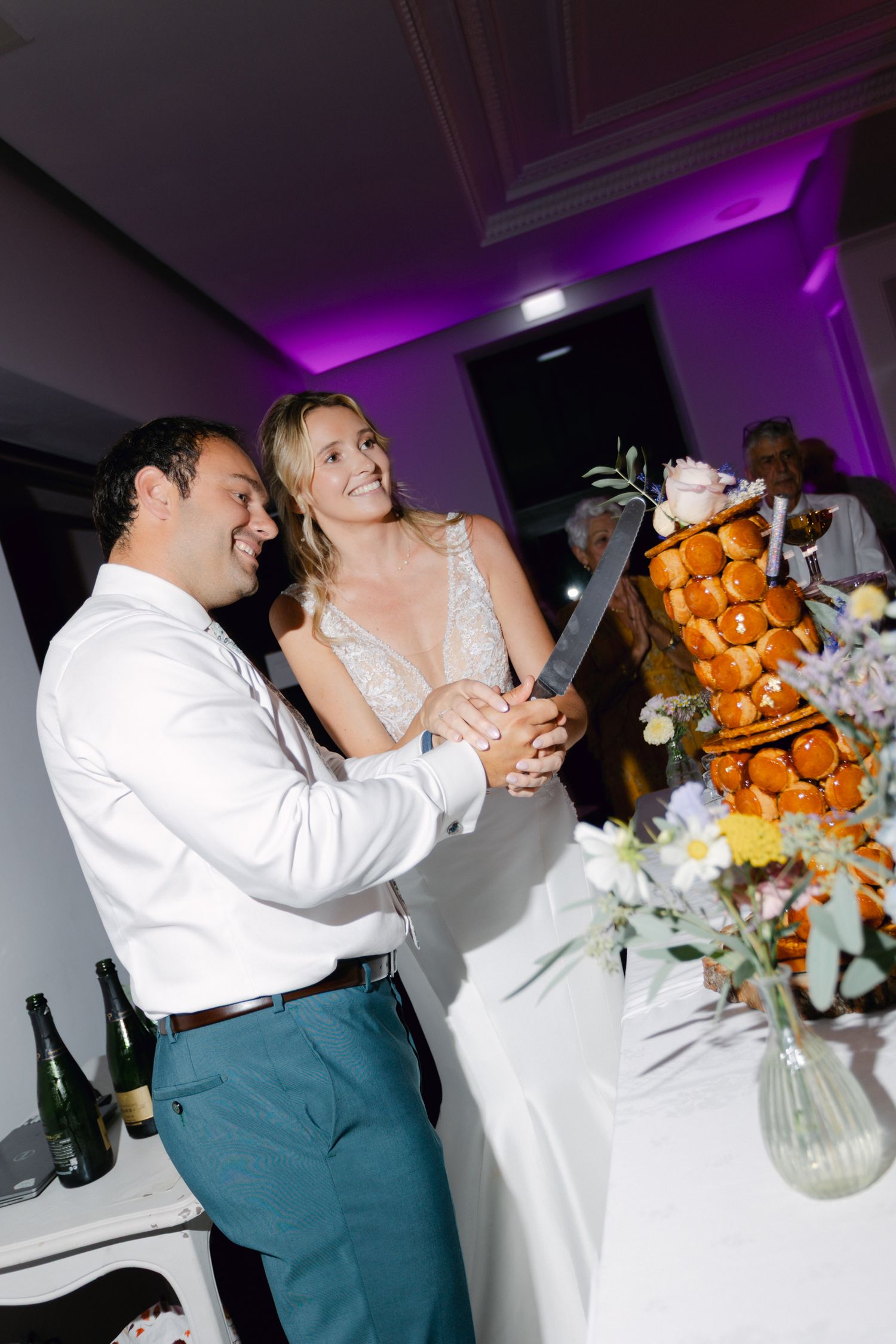La mariée et le marié souriants coupent le gâteau de mariage traditionnel de la croquembouche française sous un éclairage de réception viole