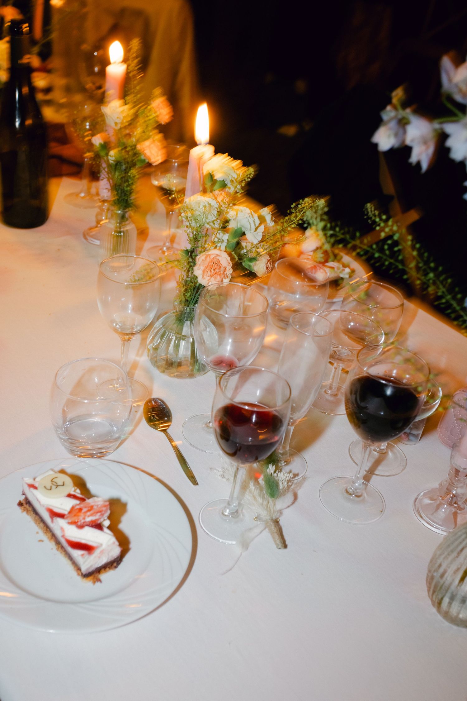Élégante table de réception de mariage avec bougies, fleurs, verres à vin et part de gâteau.