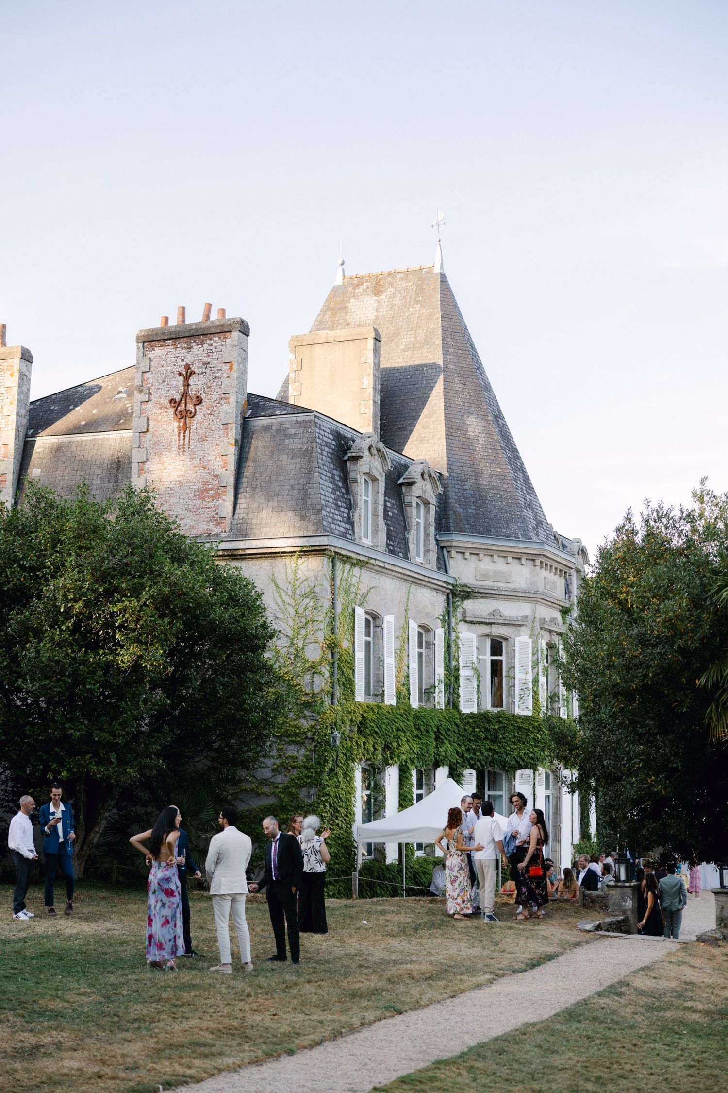 Guests mingle on the lawn of an elegant French château with ivy-covered walls and pointed turrets at a summer outdoor event.