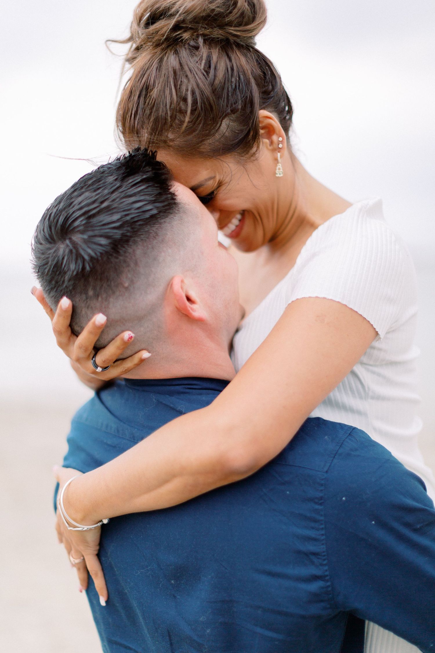 Couple s'embrassant sur la plage, femme souriante avec les bras autour du cou de l'homme, portant une bague de fiançailles.