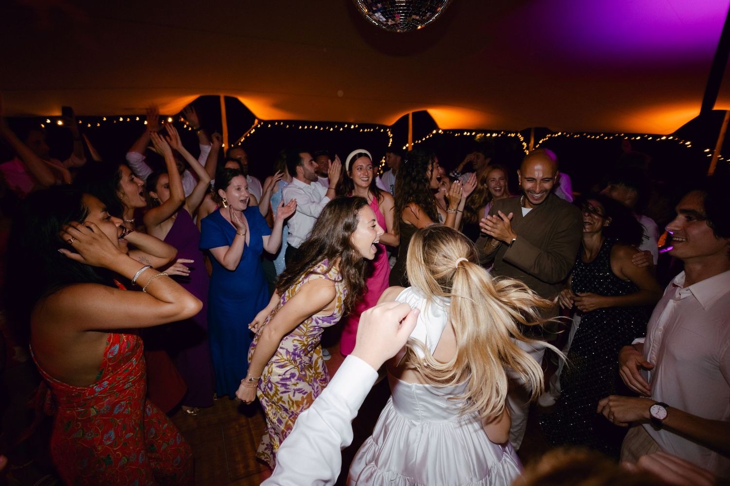 Une foule énergique d'invités au mariage dansant ensemble sous des lumières chaudes lors de la célébration de la réception.