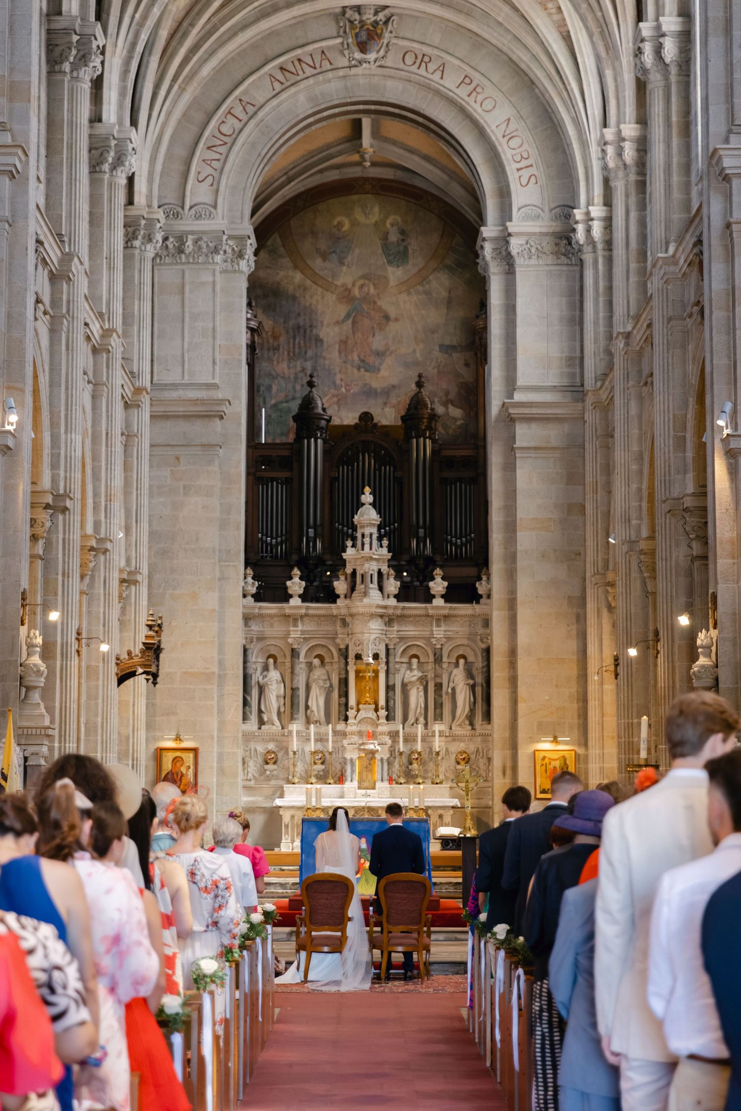 Élégante cérémonie de mariage à l'église avec des invités assis sur des bancs, un autel orné, un orgue à tuyaux et des fresques religieuses