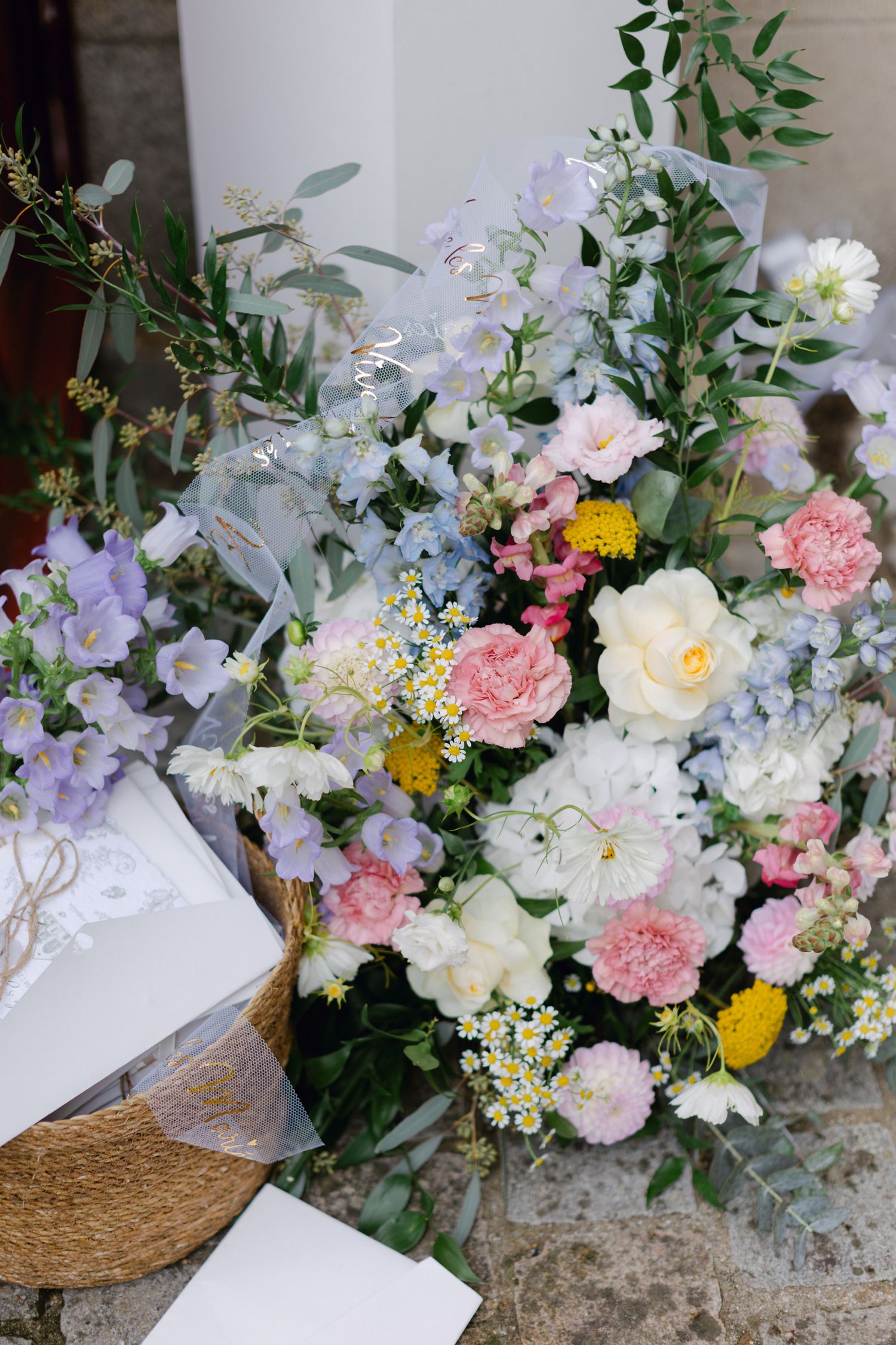 Un arrangement floral pastel luxuriant avec des fleurs roses, blanches, lavande et jaunes décore l'entrée de l'église.