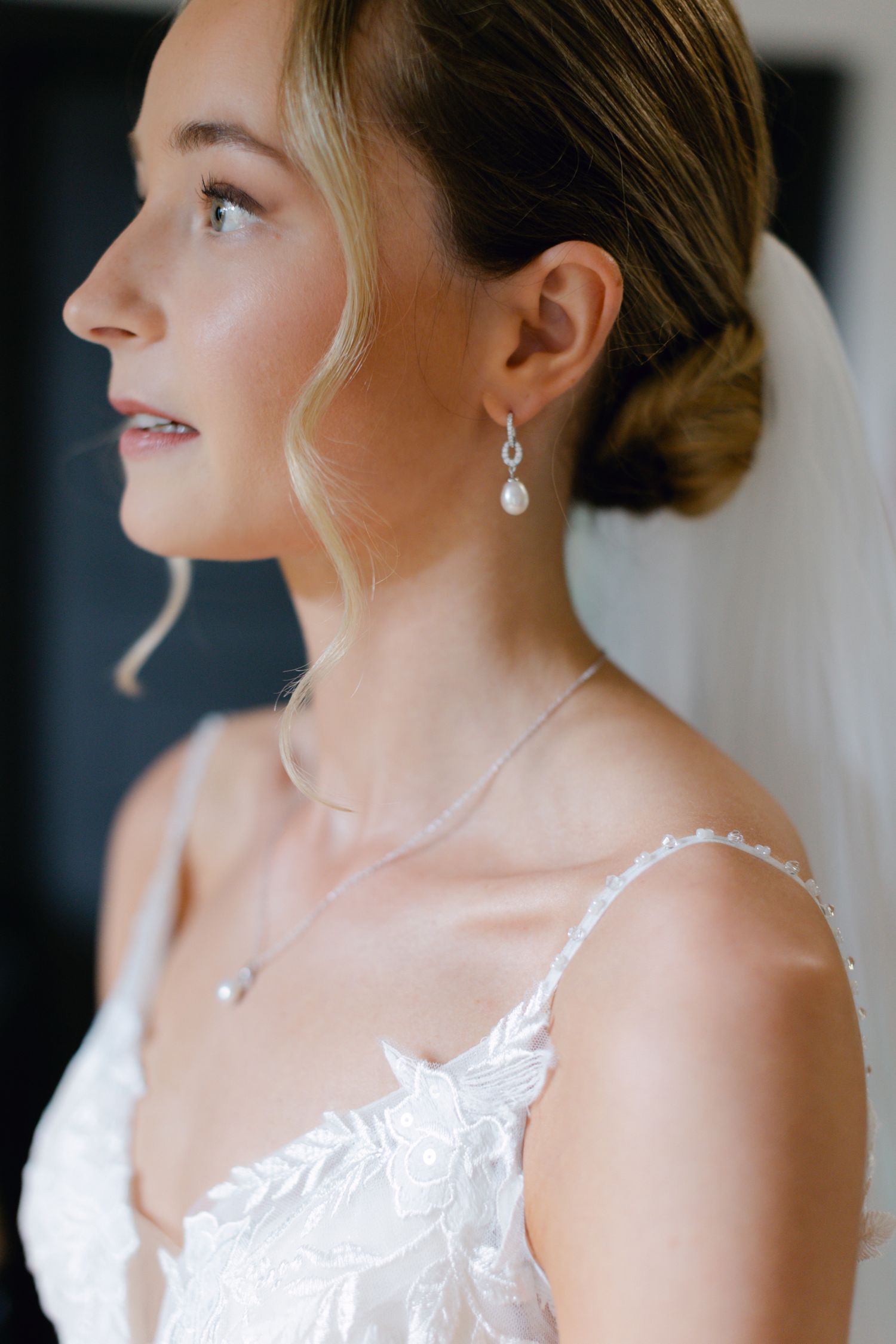 Profil en gros plan d'une mariée portant des boucles d'oreilles en perles et une robe de mariée en dentelle avec voile.