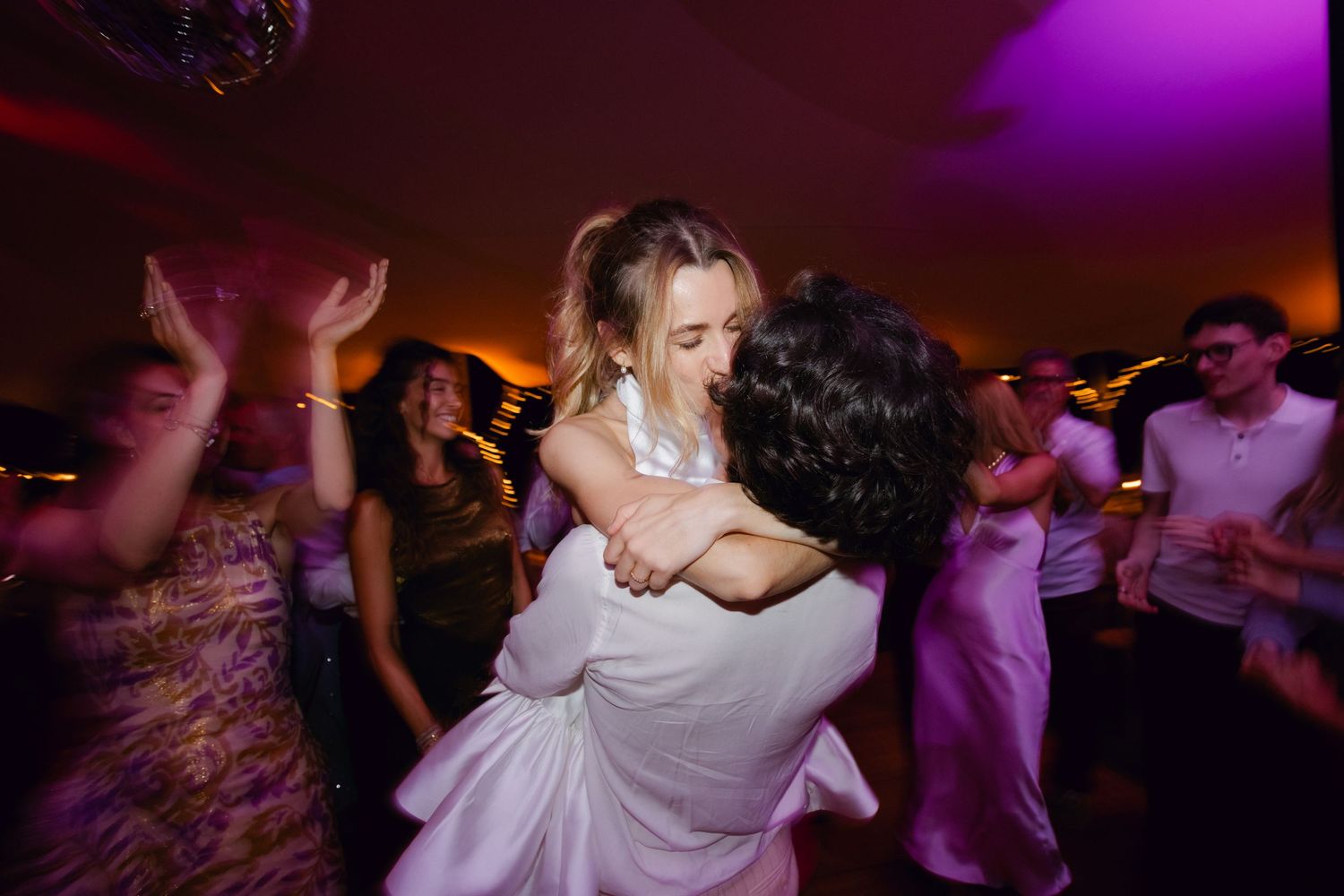 La mariée en robe blanche est soulevée et embrassée par l'invité sur la piste de danse de mariage vibrante.