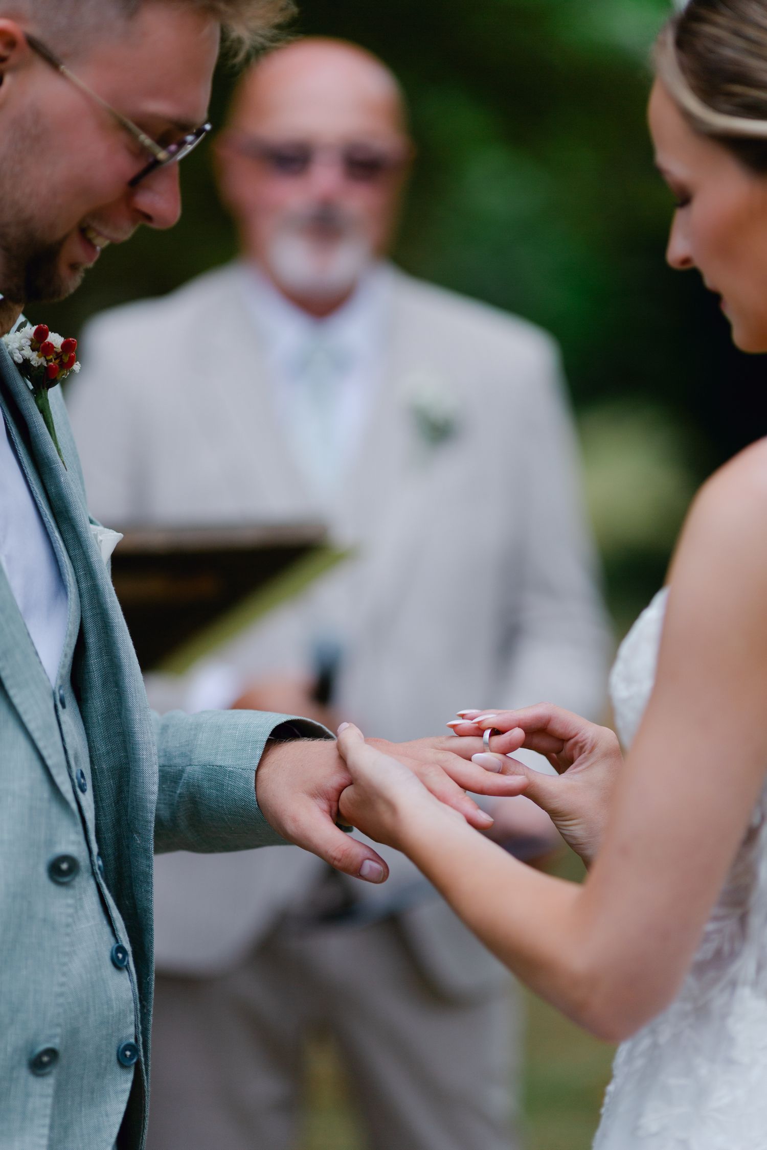 La mariée place une alliance sur le doigt du marié lors d'une cérémonie en plein air tandis que l'officiant se tient en arrière-plan.
