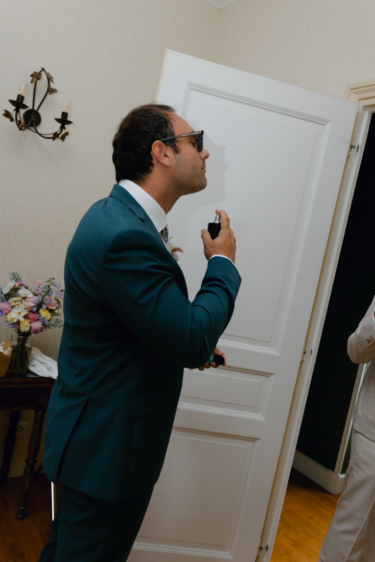 Marié en costume sarcelle appliquant de l'eau de Cologne tout en se préparant pour la cérémonie de mariage à l'intérieur.