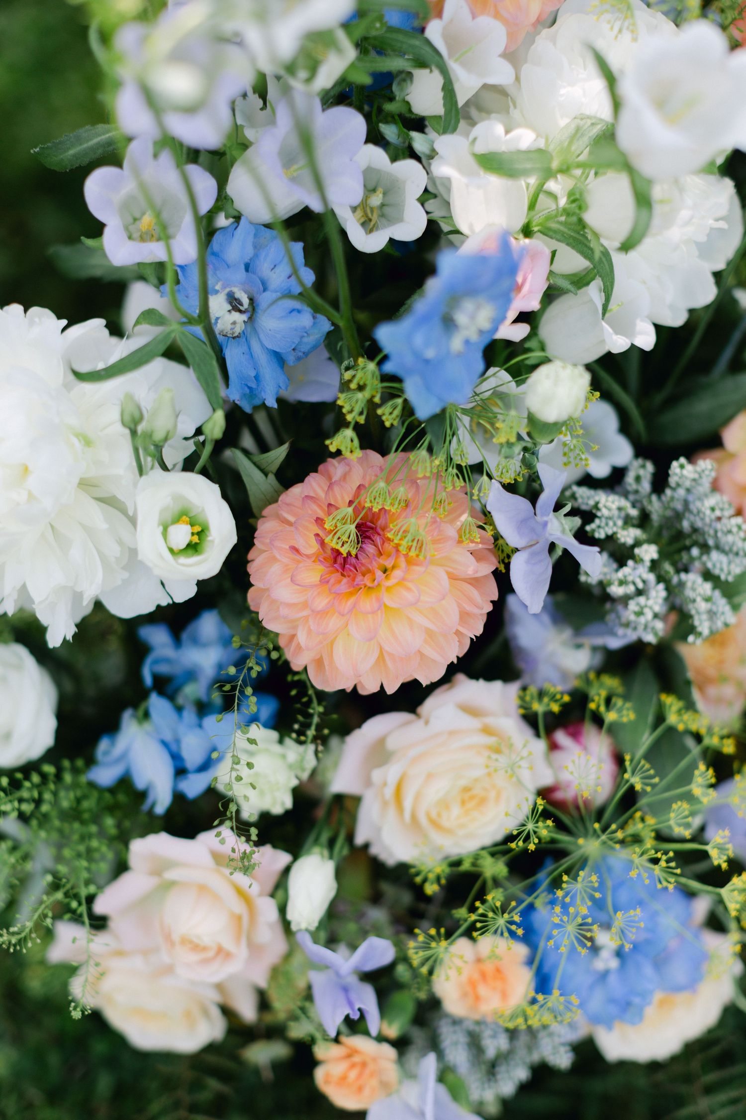Gros plan d'un bouquet de mariage élégant avec dahlia pêche, roses crème, delphinium bleu et fleurs blanches sur herbe verte.