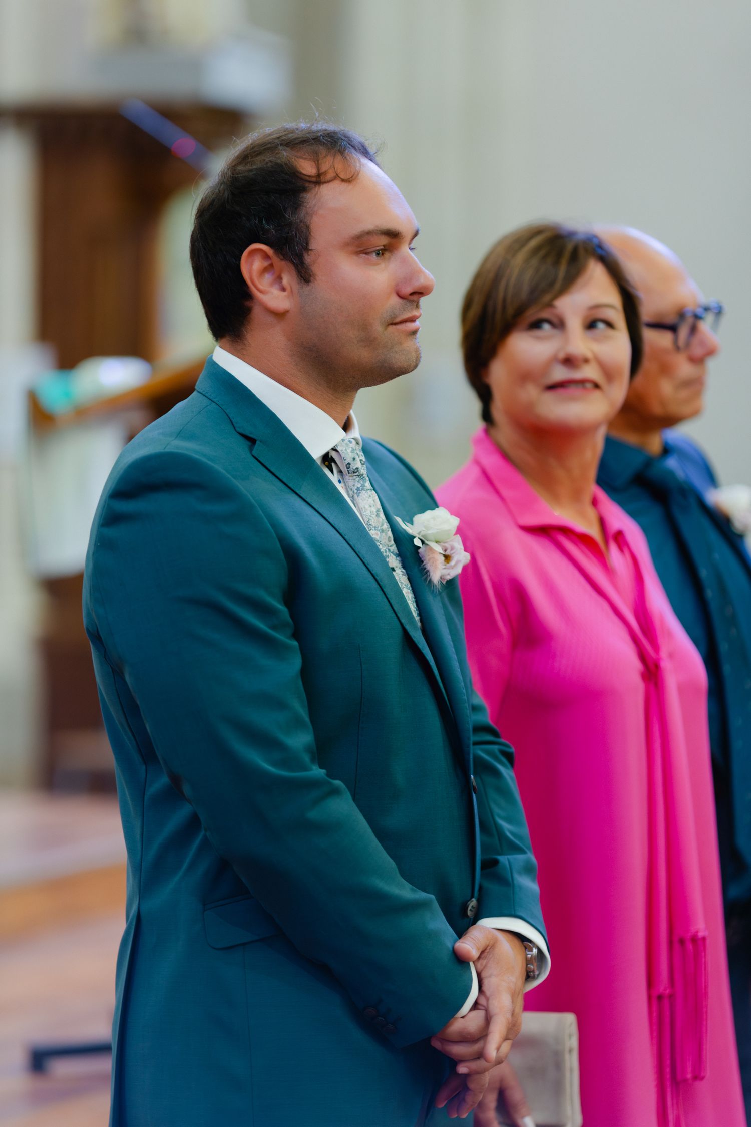 Le marié en costume sarcelle avec boutonnière se tient à l'autel à côté d'une femme en robe rose lors de la cérémonie de mariage.