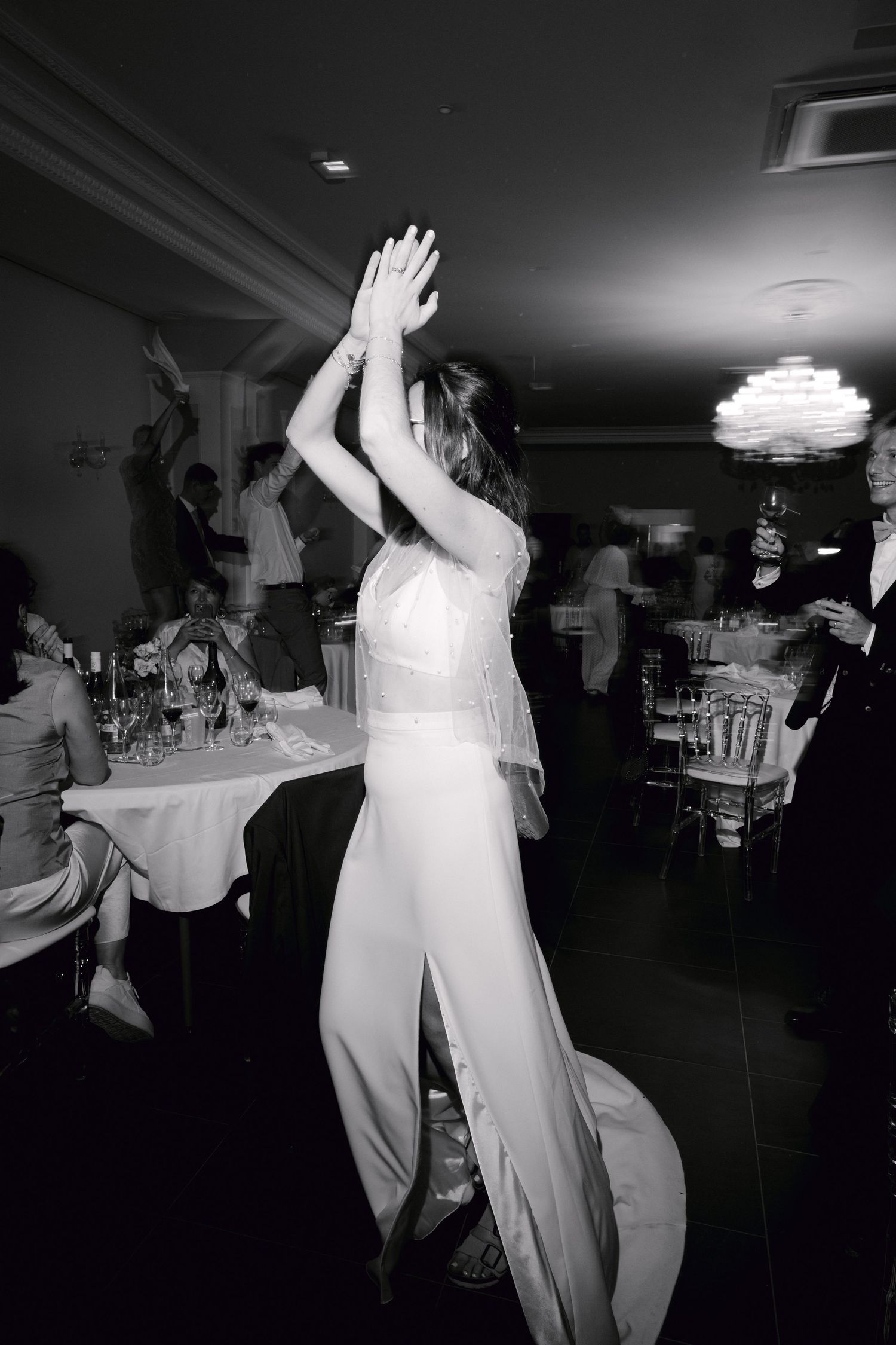 Photo en noir et blanc d'une mariée dansant les bras levés lors de sa réception de mariage.