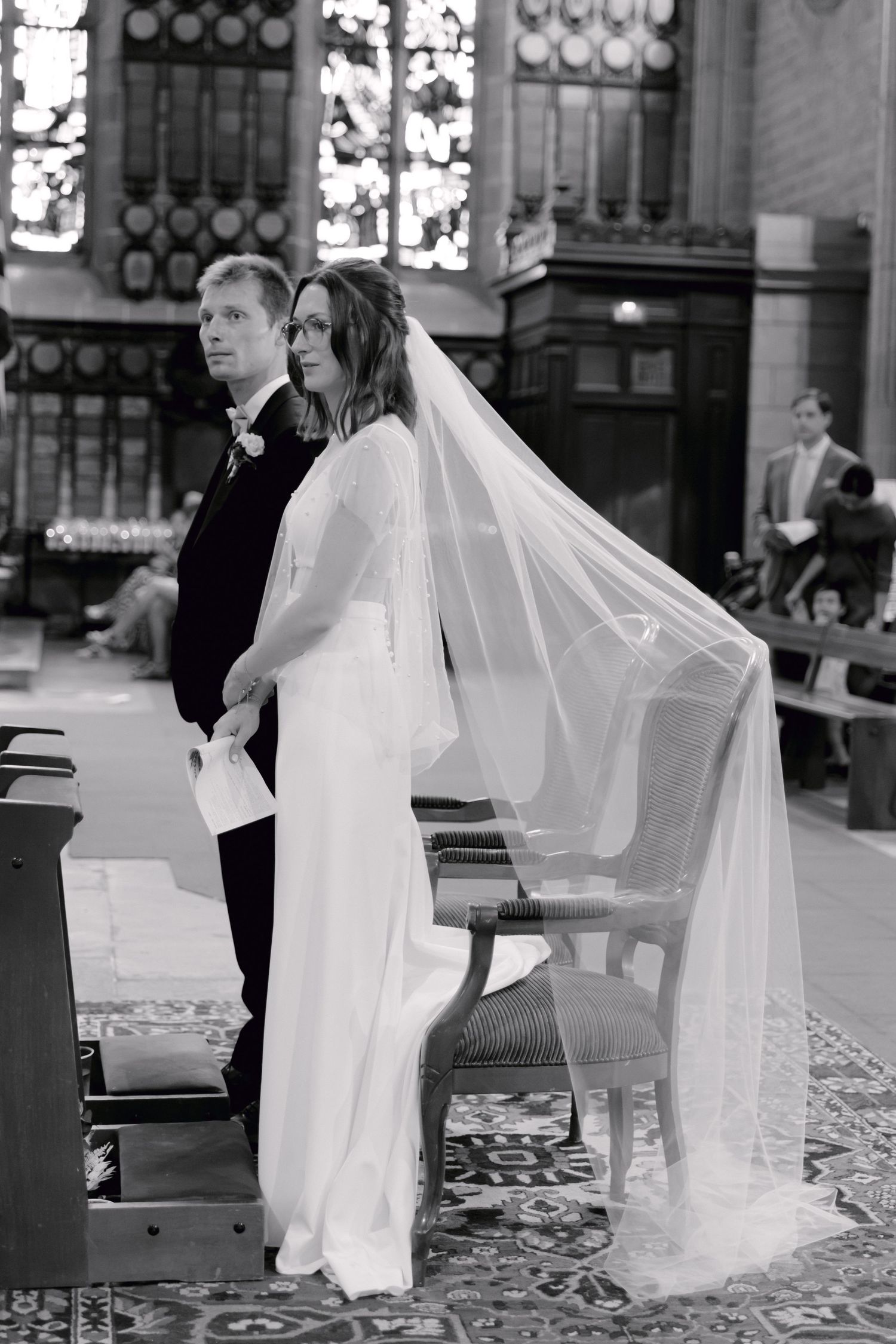 Photo en noir et blanc d'une mariée dans un voile fluide et du marié debout à l'autel lors d'une cérémonie de mariage à l'église.