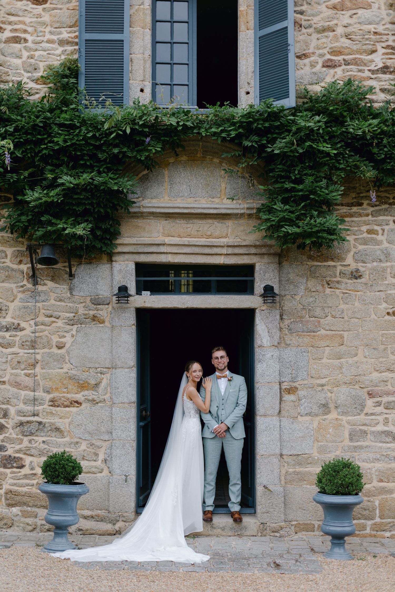 La mariée et le marié posent élégamment dans la porte arquée d'un charmant château en pierre le jour du mariage.