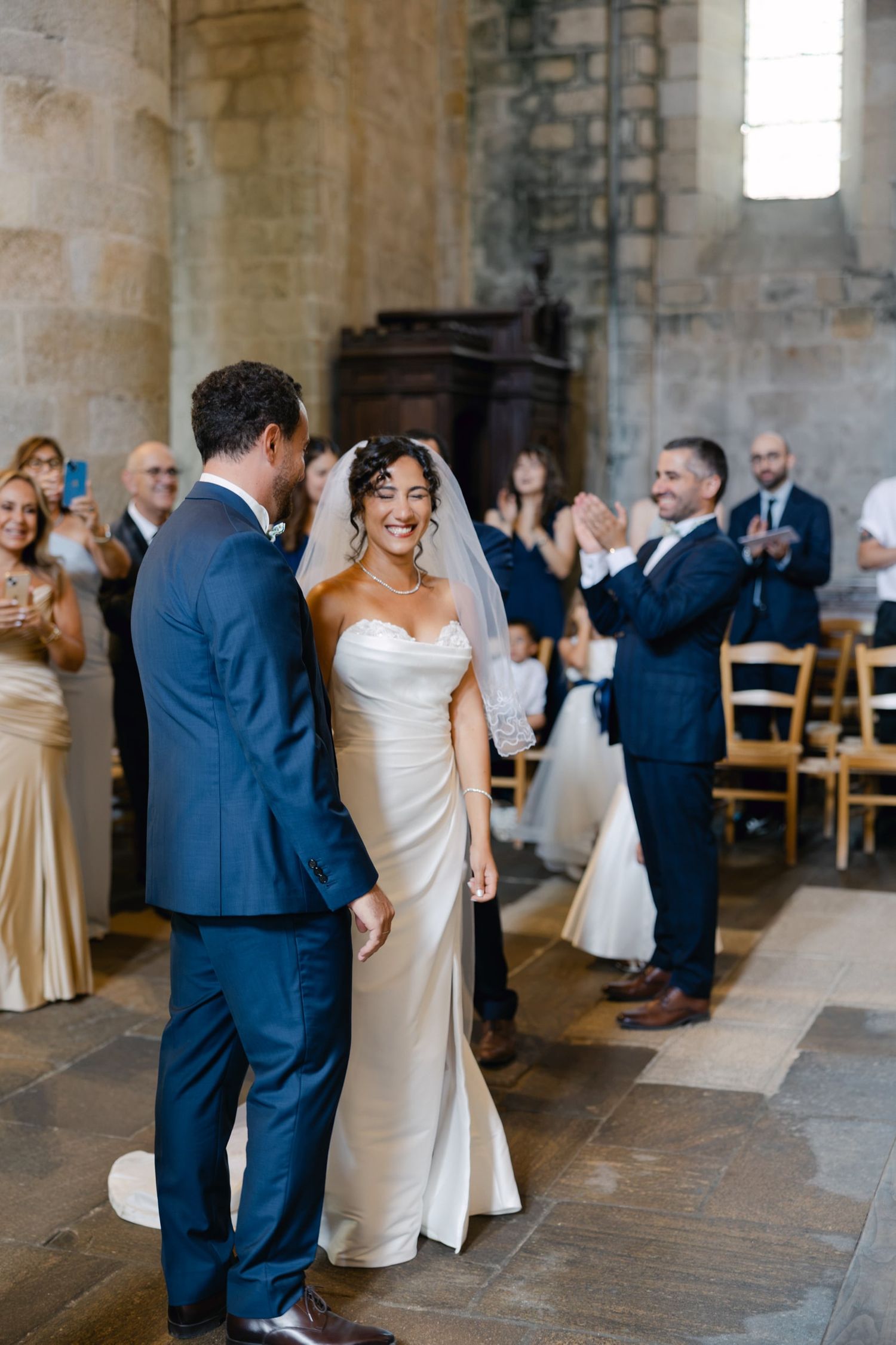 Bride and groom walk down the aisle as guests applaud in a stunning stone church wedding ceremony.