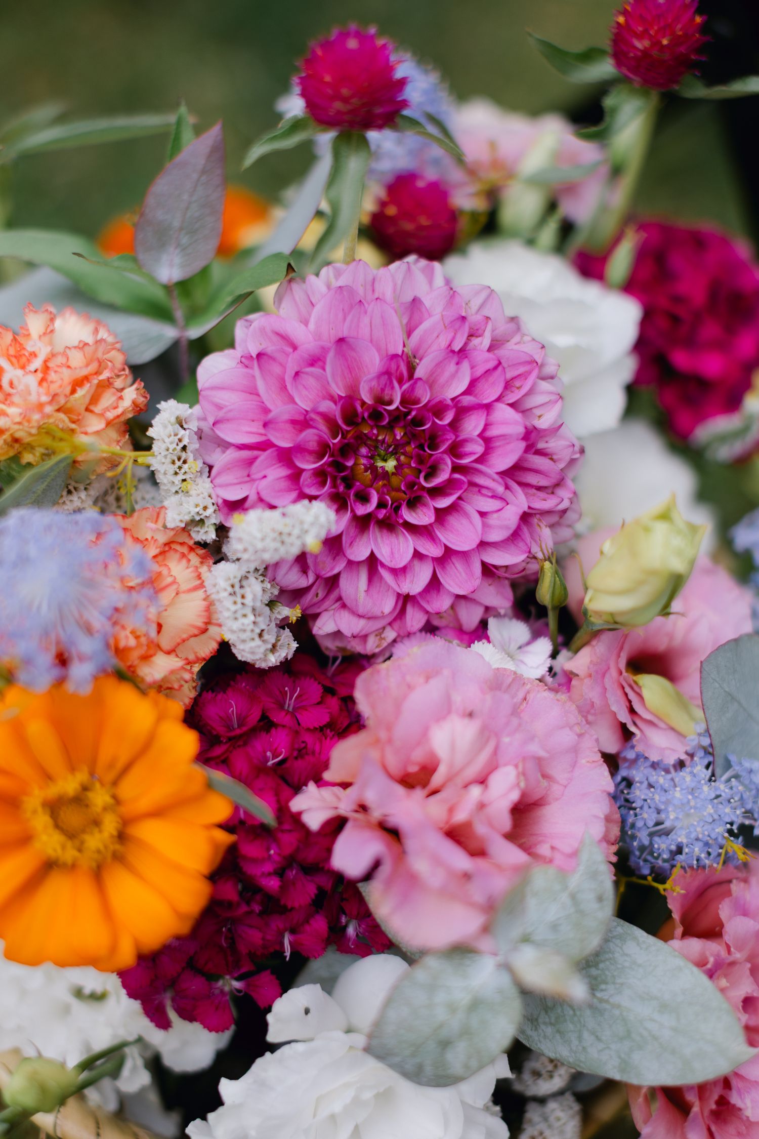 Bouquet de mariée vibrant avec des dahlias roses, des zinnias orange, des œillets magenta et de l'eucalyptus.