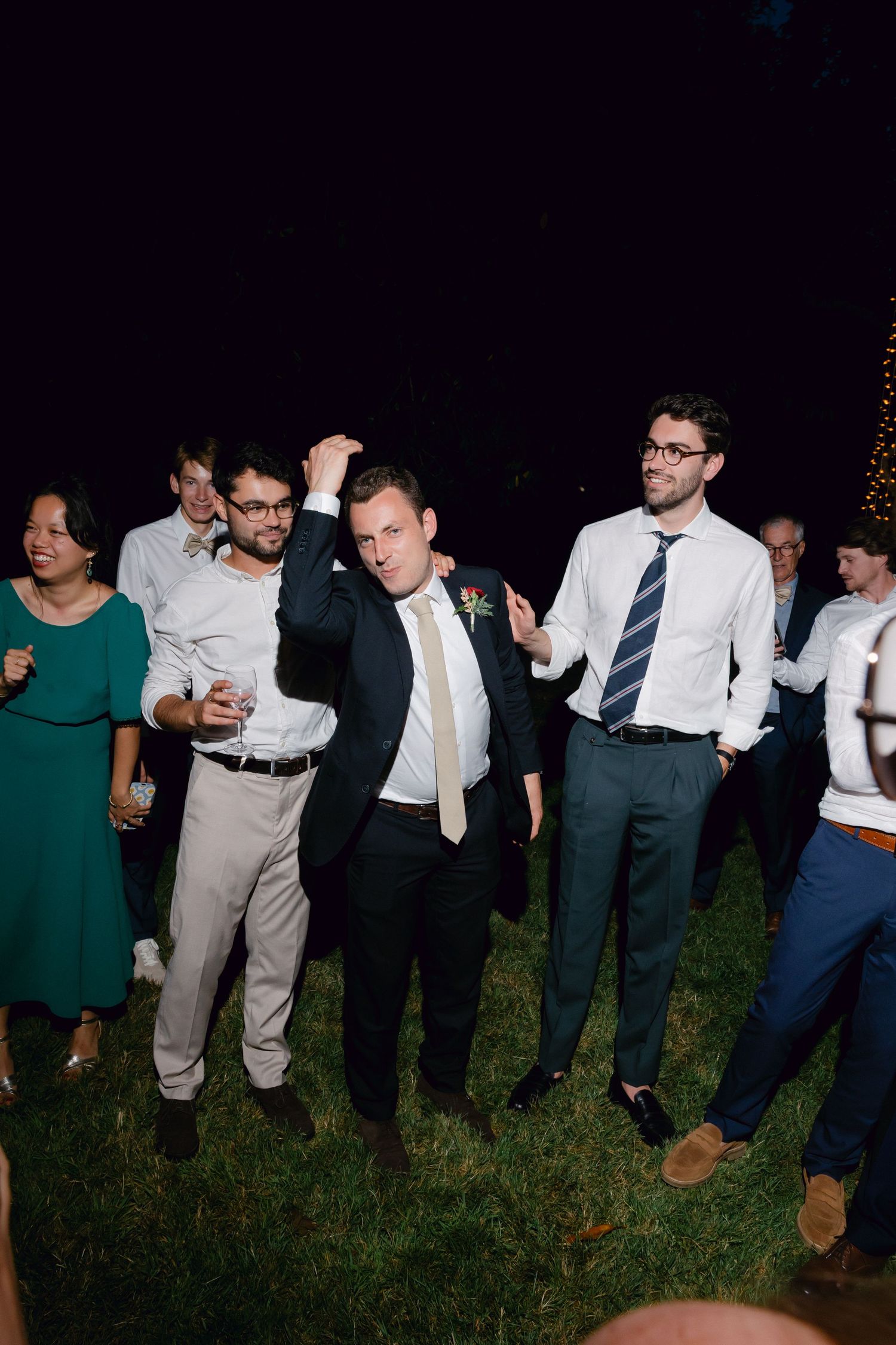 Des invités dansant et célébrant à l'extérieur lors d'une réception de mariage nocturne sur une pelouse herbeuse.