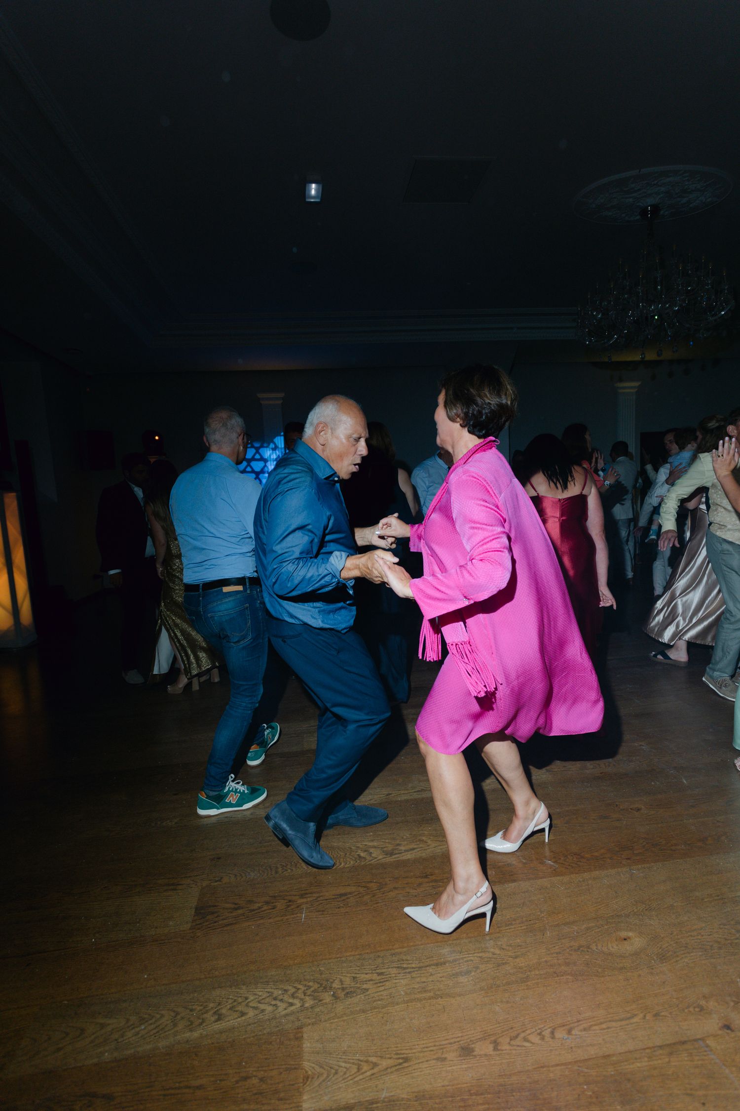 Couple dansant énergiquement à la réception de mariage, femme en tenue rose vif et homme en costume bleu.