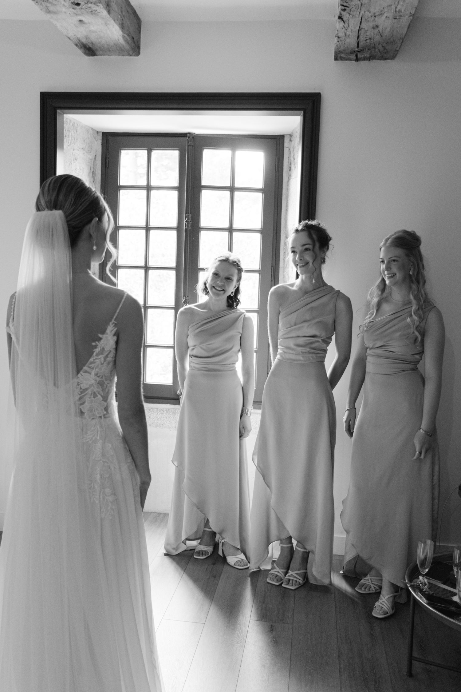 Photo en noir et blanc de la mariée révélant sa robe de mariée aux demoiselles d'honneur souriantes en robes élégantes.