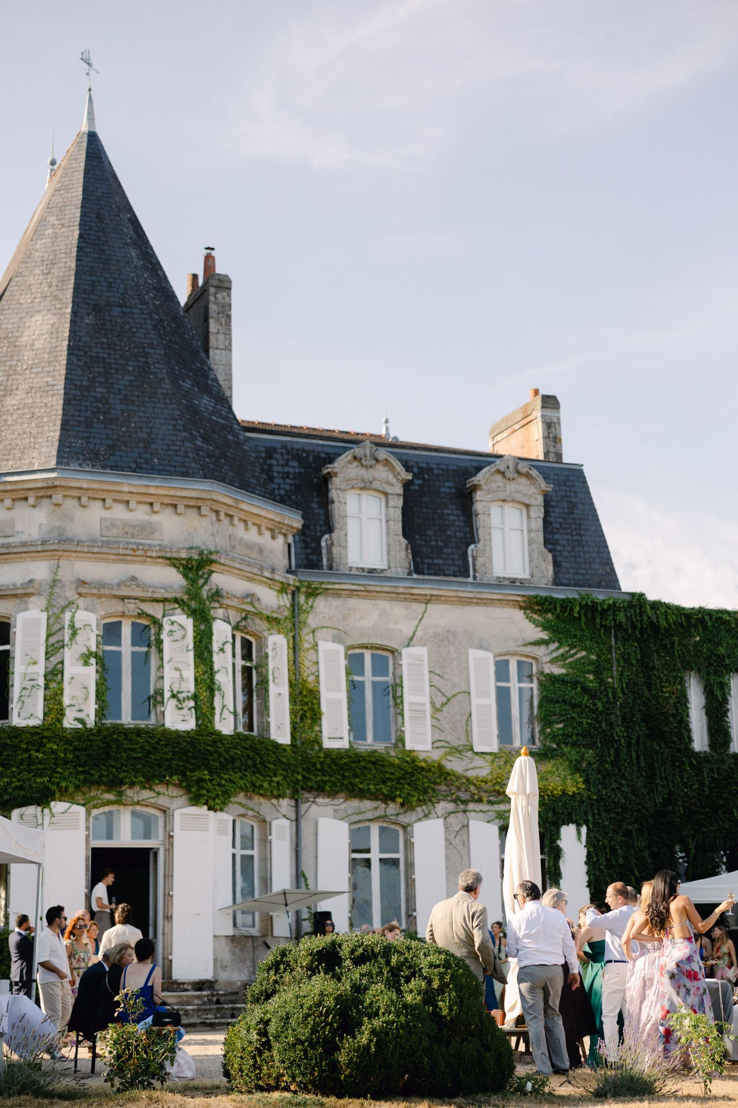 Elegant French château with ivy-covered walls and guests gathered outside for a summer wedding reception.