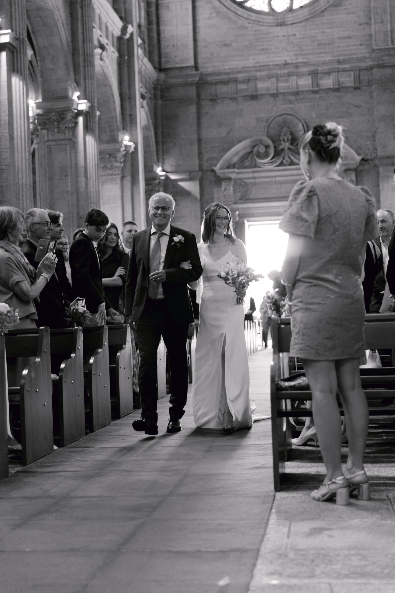 Photo en noir et blanc d'une mariée marchant dans l'allée de l'église avec son père lors d'une cérémonie de mariage traditionnelle.