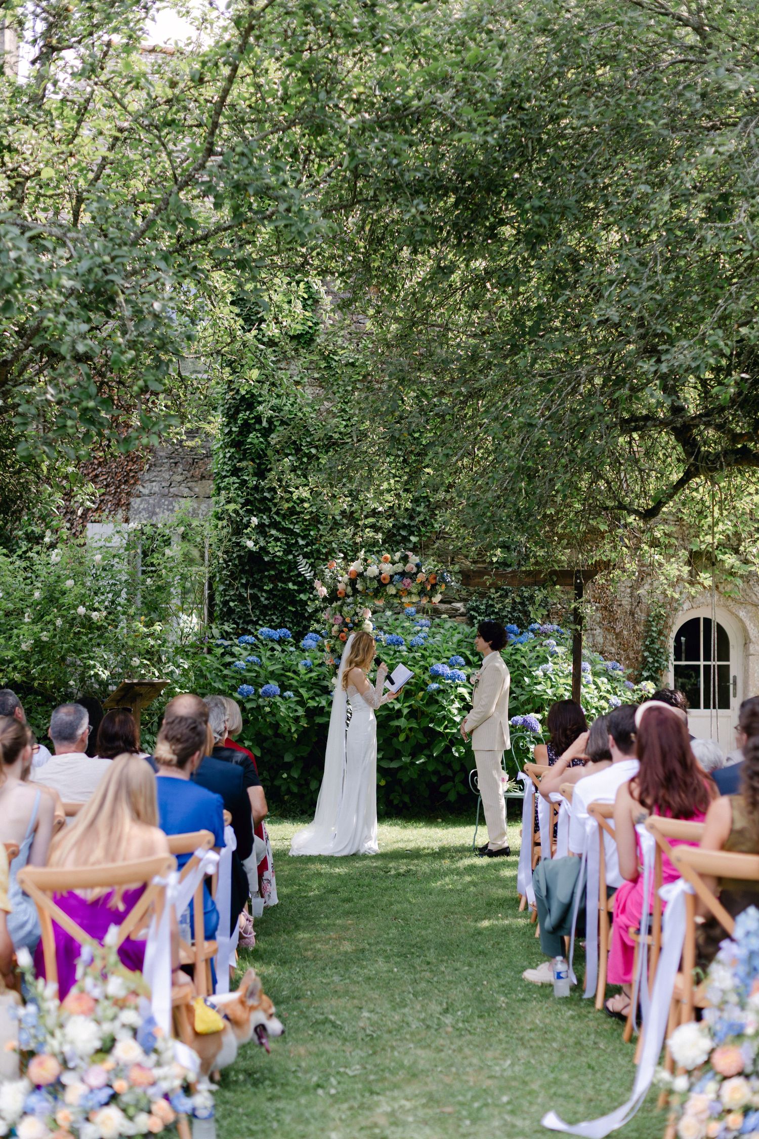 Plan d'une cérémonie de mariage dans le jardin extérieur avec des invités assis le long de l'allée alors que le couple échange des vœux.