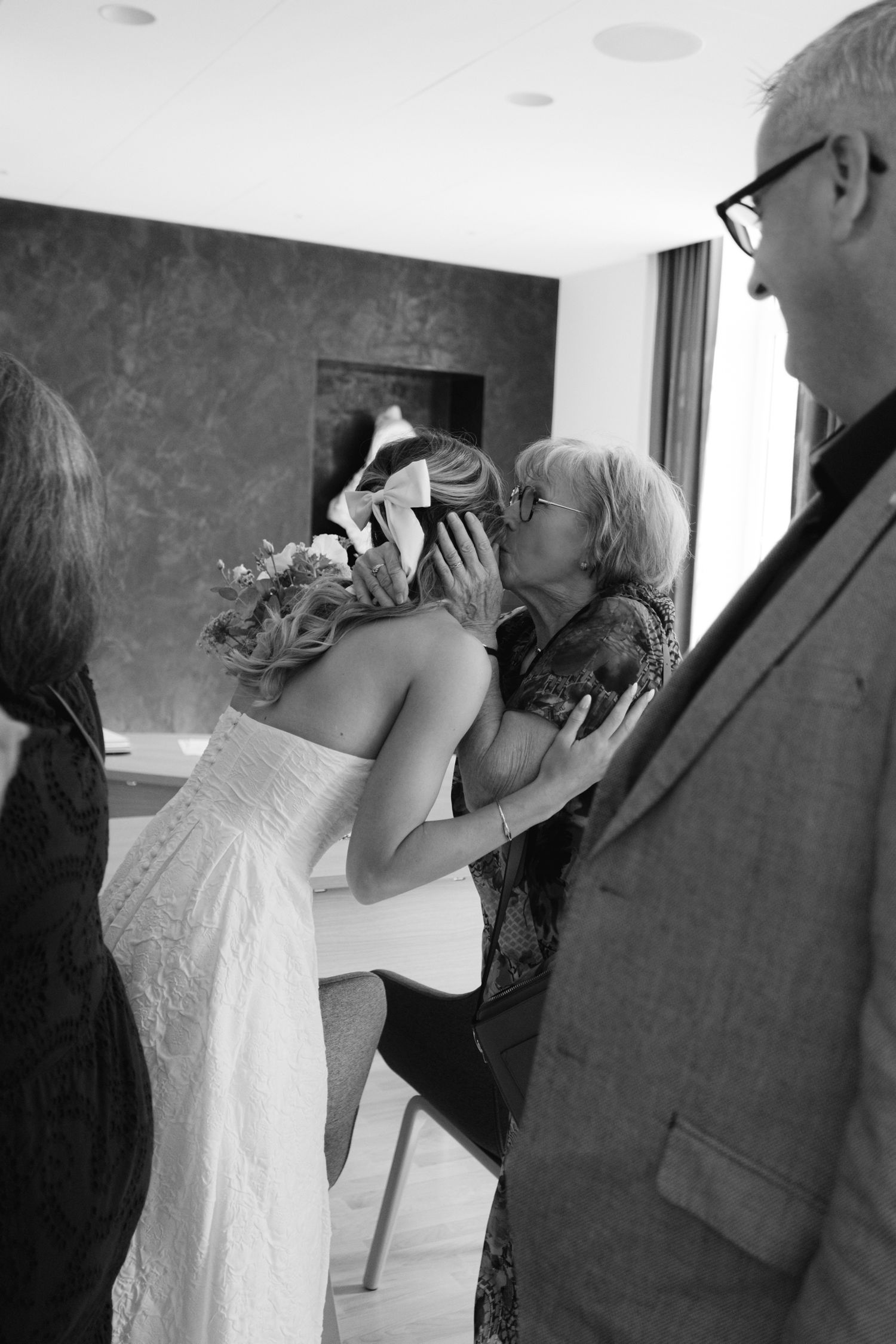 Photo en noir et blanc de la mariée recevant un baiser d'une invitée âgée après la cérémonie de mariage.