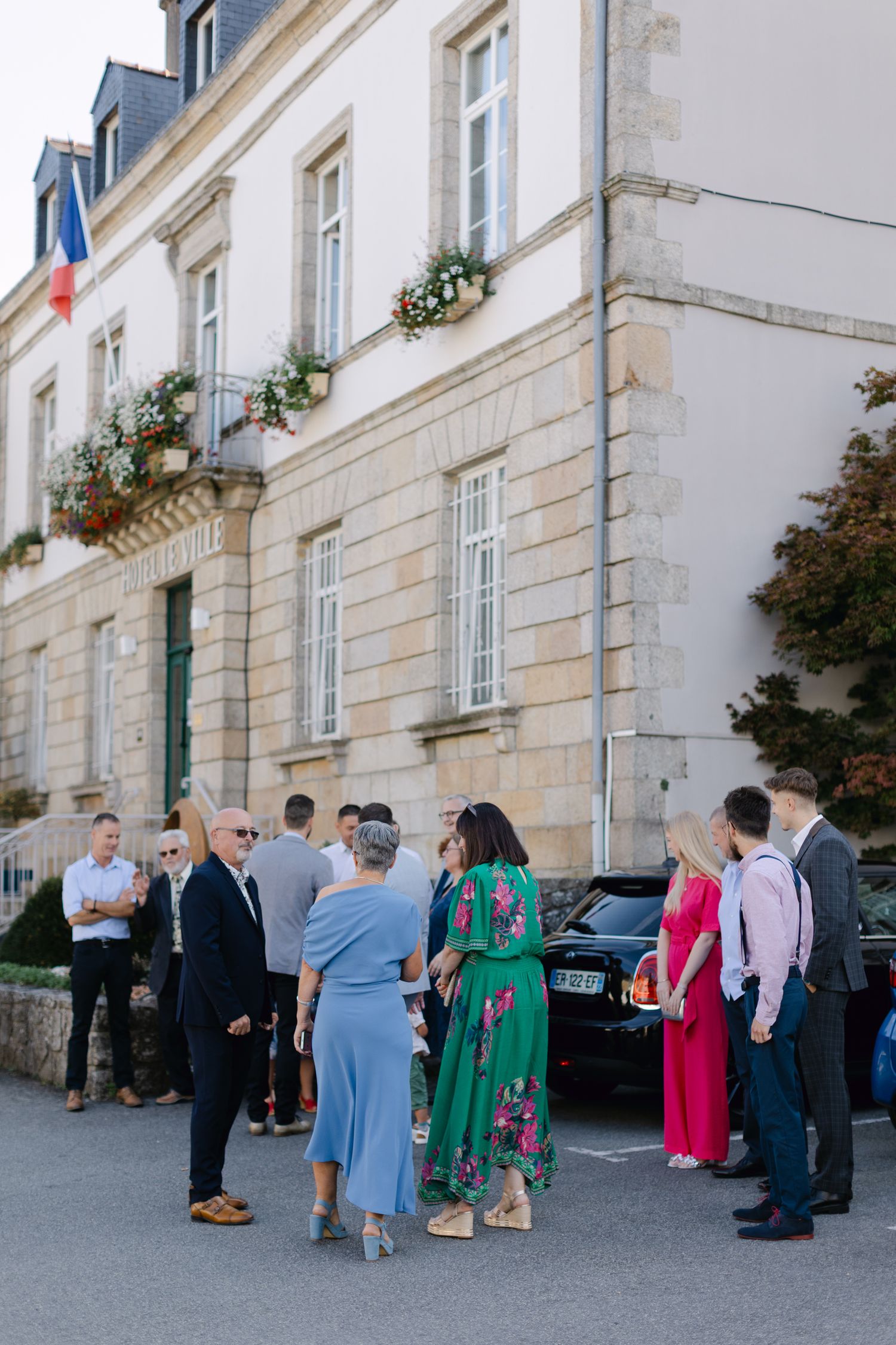 Les invités au mariage se rassemblent à l'extérieur d'un bâtiment en pierre français classique avant la cérémonie.