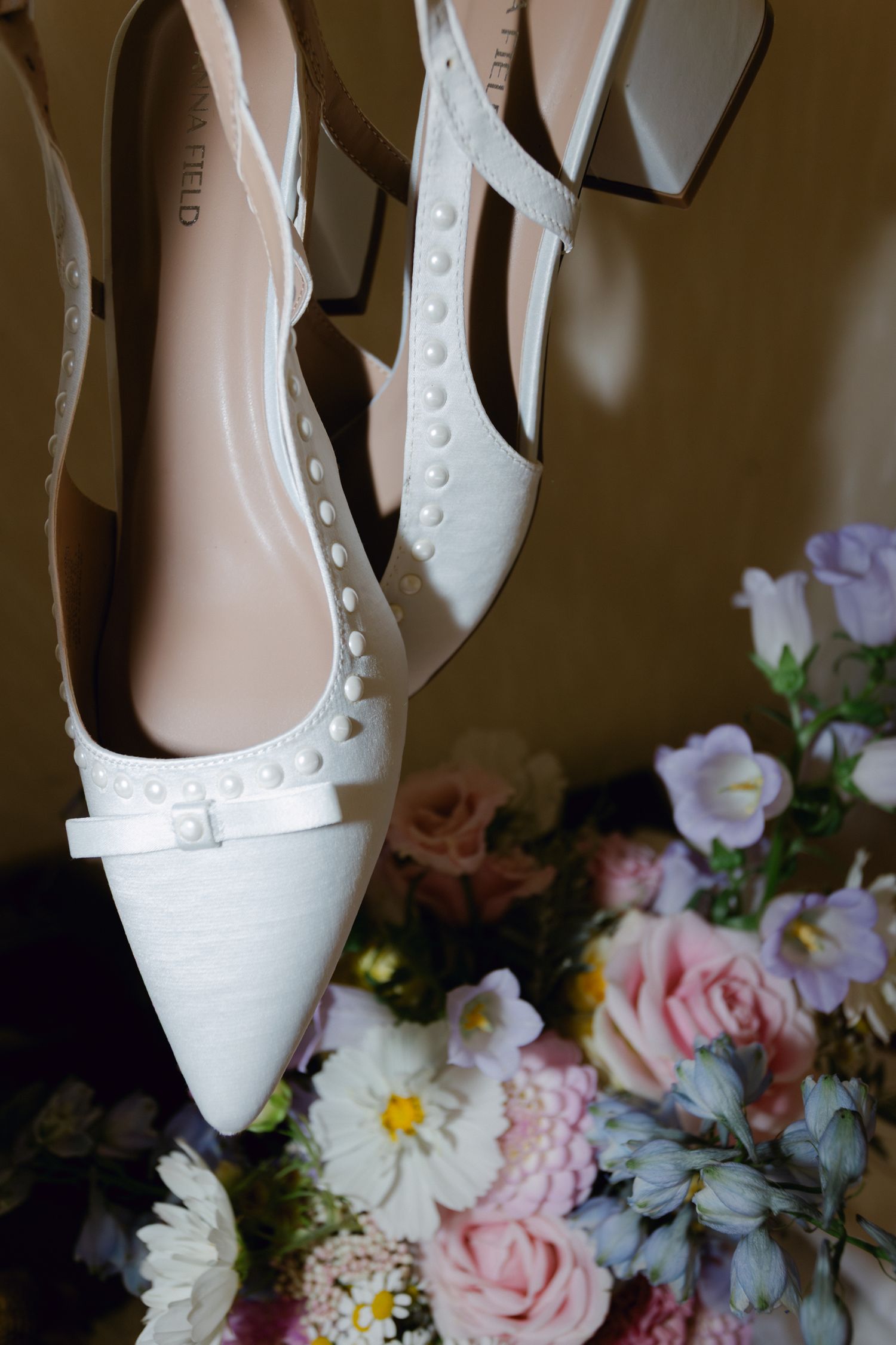 Talons de mariée Karl Lagerfeld blancs avec des détails perlés exposés au-dessus d'un bouquet floral coloré.
