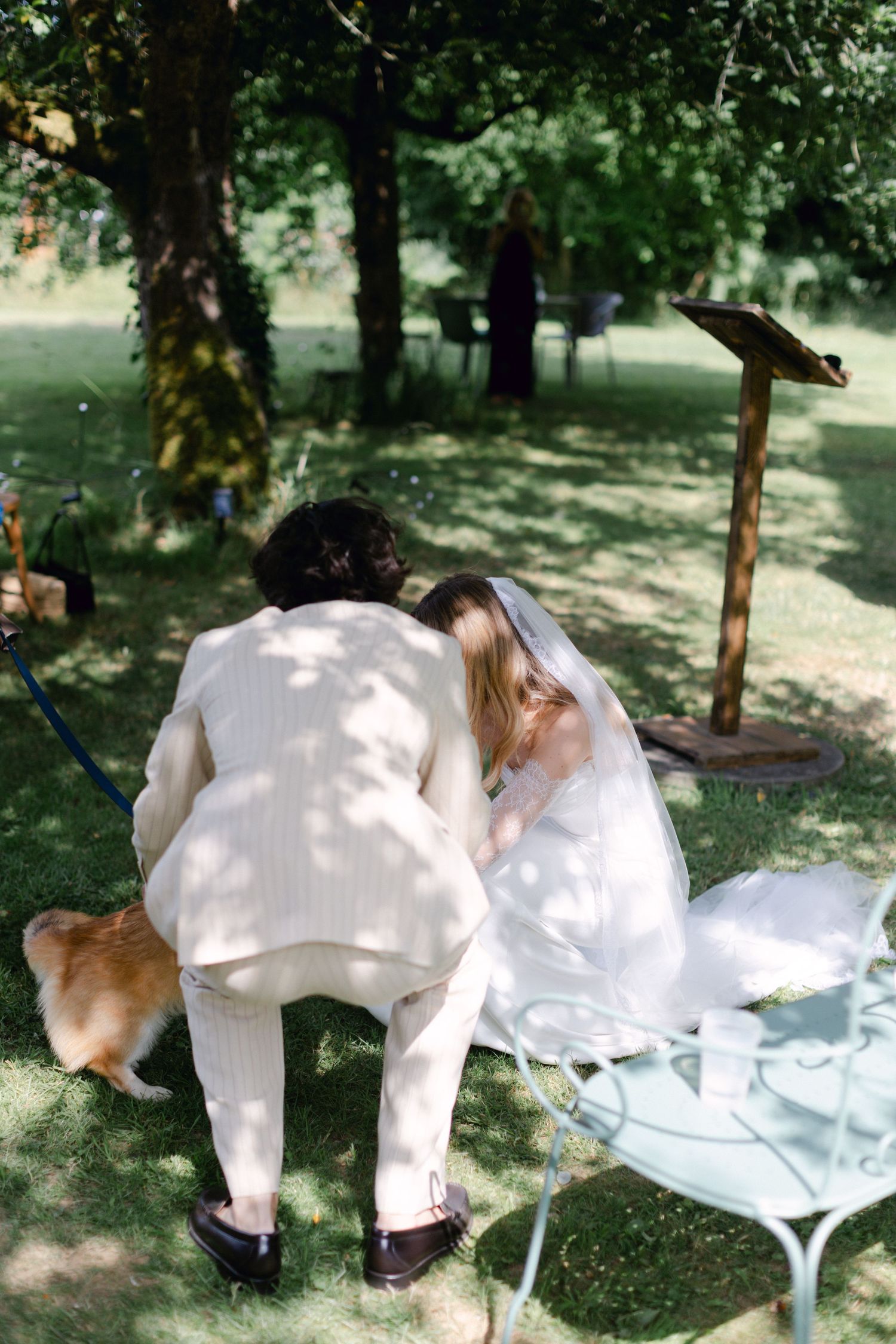 La mariée et le marié se penchent ensemble tout en saluant un adorable chien corgi lors de leur cérémonie de mariage en plein air.