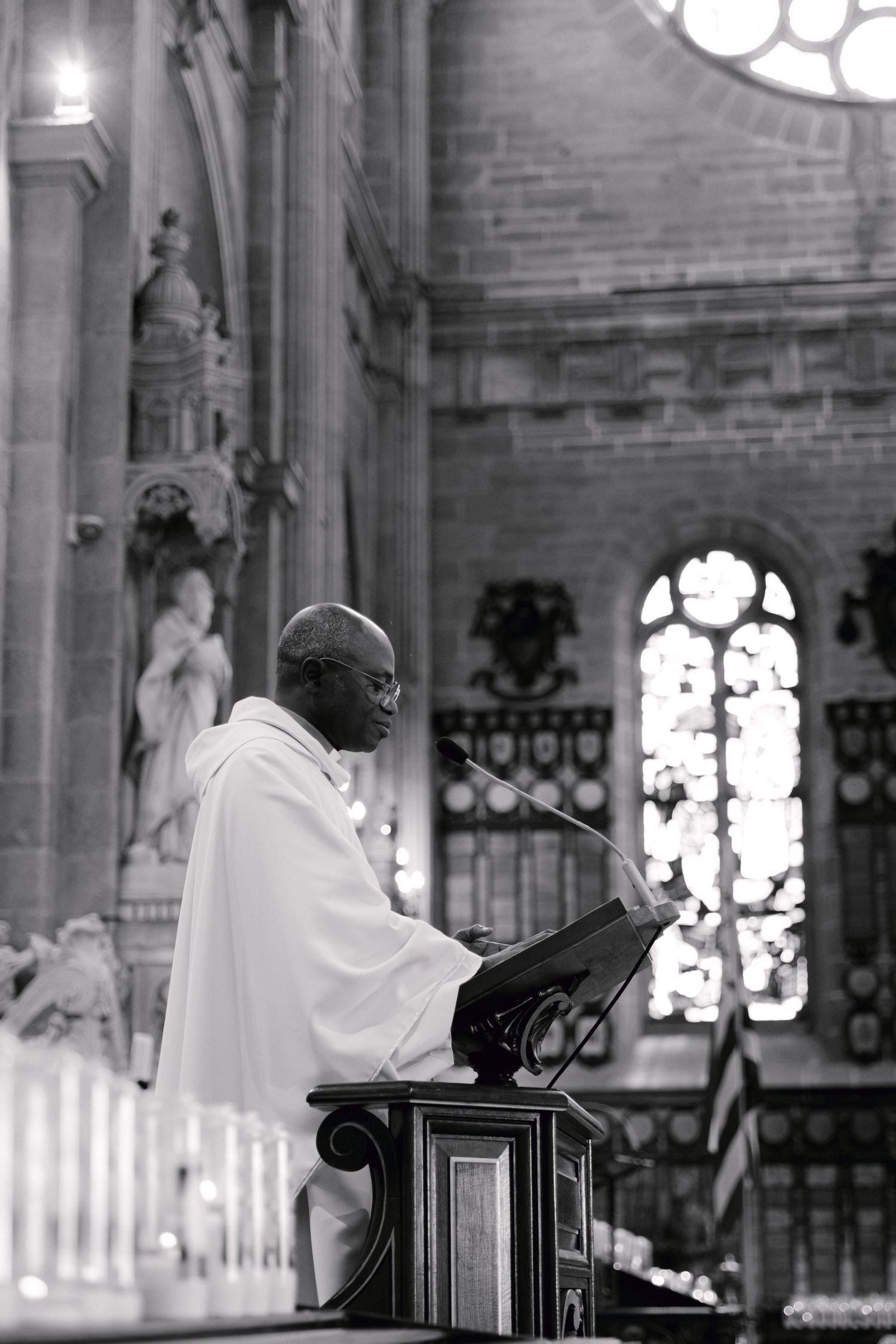 Photo en noir et blanc d'un prêtre prononçant un sermon à une chaire à l'intérieur d'une grande cathédrale avec des vitraux.
