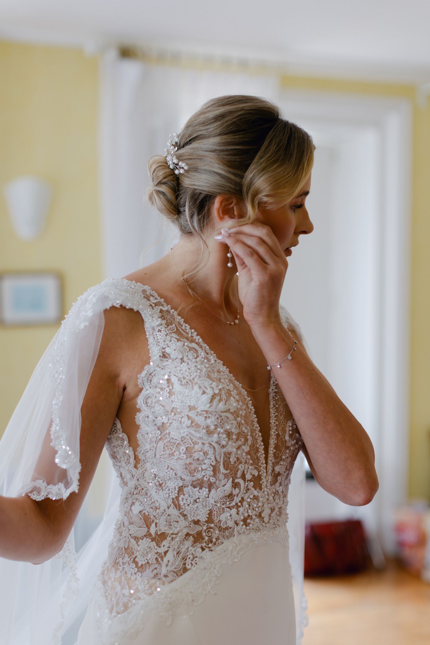 Mariée élégante en robe de mariée en dentelle mettant des boucles d'oreilles et des accessoires floraux pour cheveux.