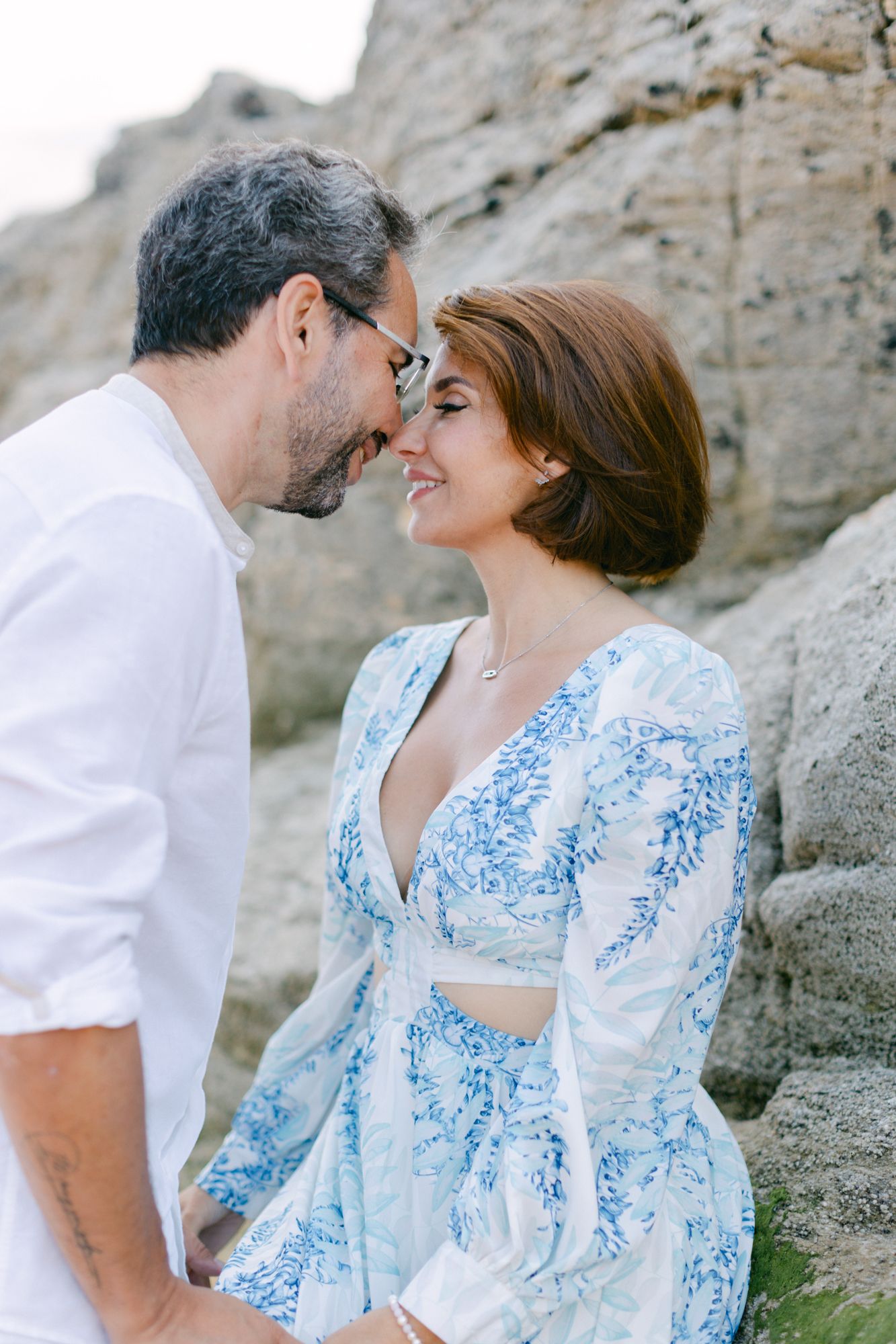 Un couple en tenue romantique partage un tendre moment nez à nez près des falaises rocheuses à l'extérieur.