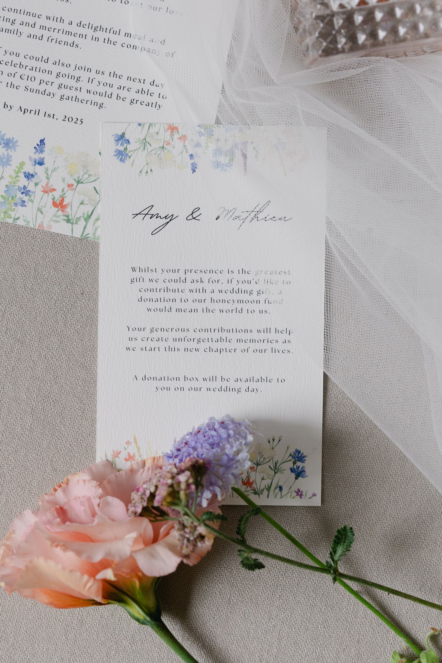 Papeterie de mariage élégante pour Amy et Mathieu entourée de fleurs roses et de tulle sur une surface grise.
