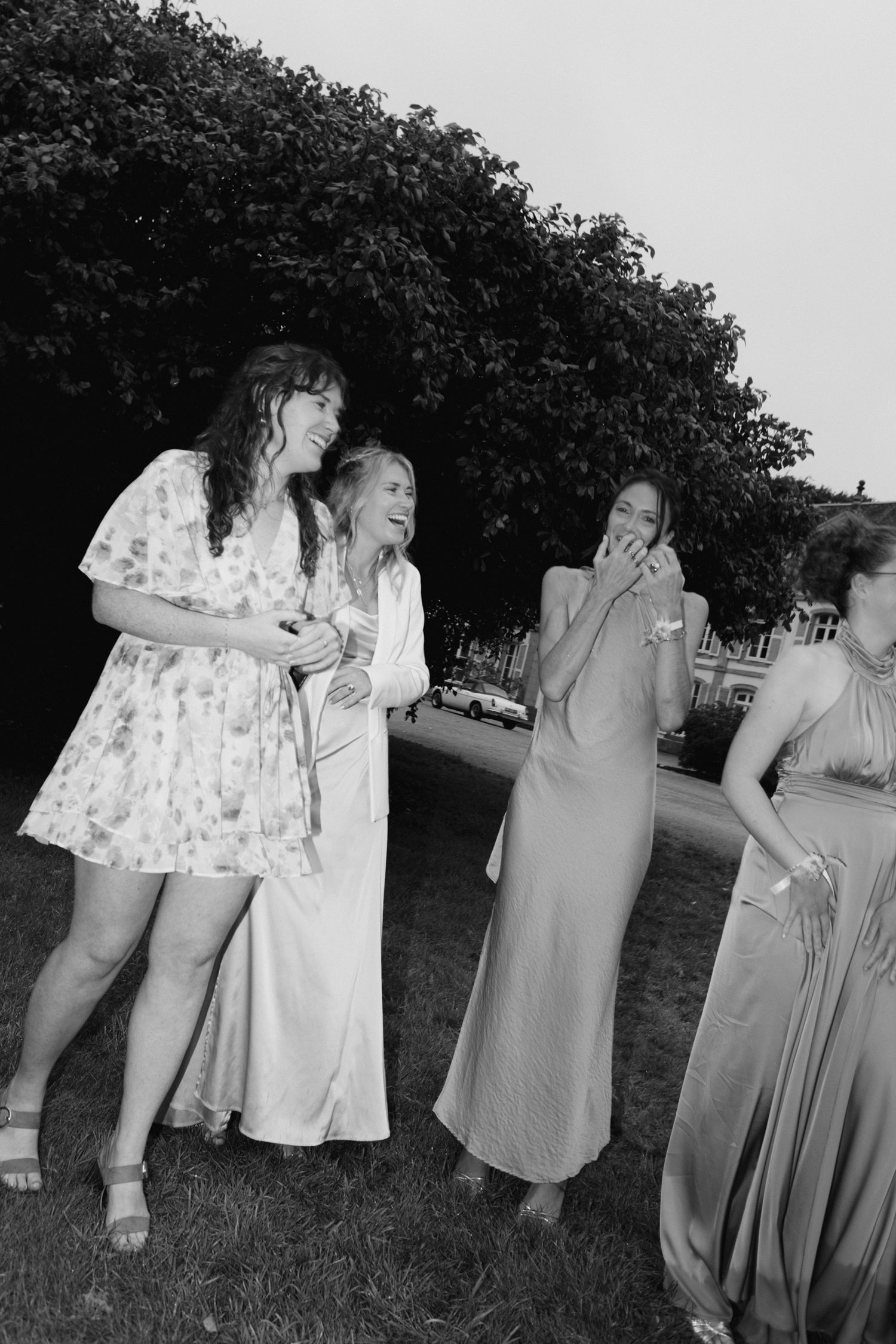 Photo en noir et blanc de quatre femmes riant ensemble à l'extérieur lors d'une célébration de mariage.