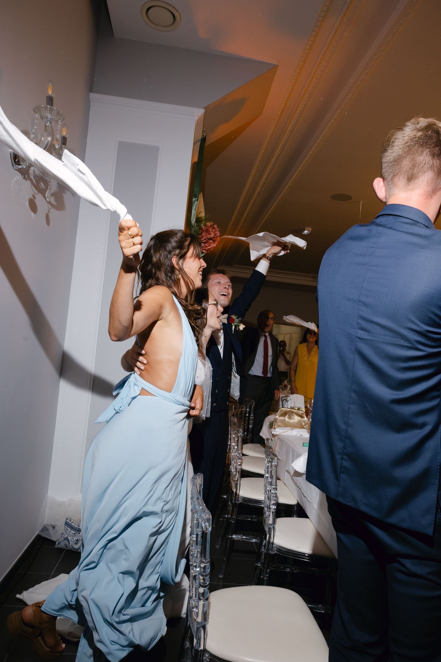 Les invités célèbrent lors d'une réception de mariage, en agitant des serviettes dans un lieu intérieur festif avec un décor élégant.