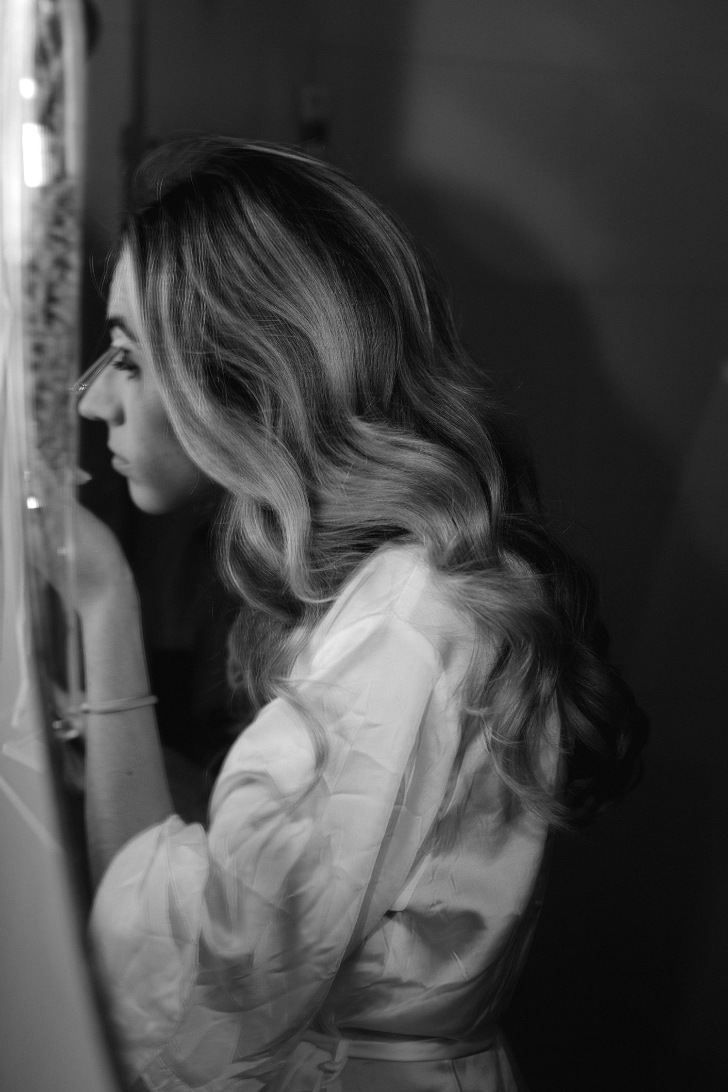Portrait de profil noir et blanc d'une mariée aux cheveux blonds ondulés dans une robe de satin blanc.