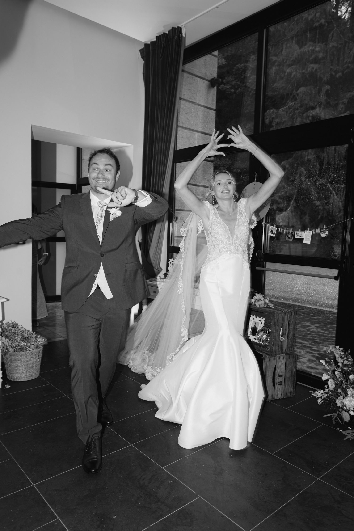 Photo en noir et blanc de la mariée et du marié faisant une grande entrée, dansant joyeusement lors de la réception de mariage.