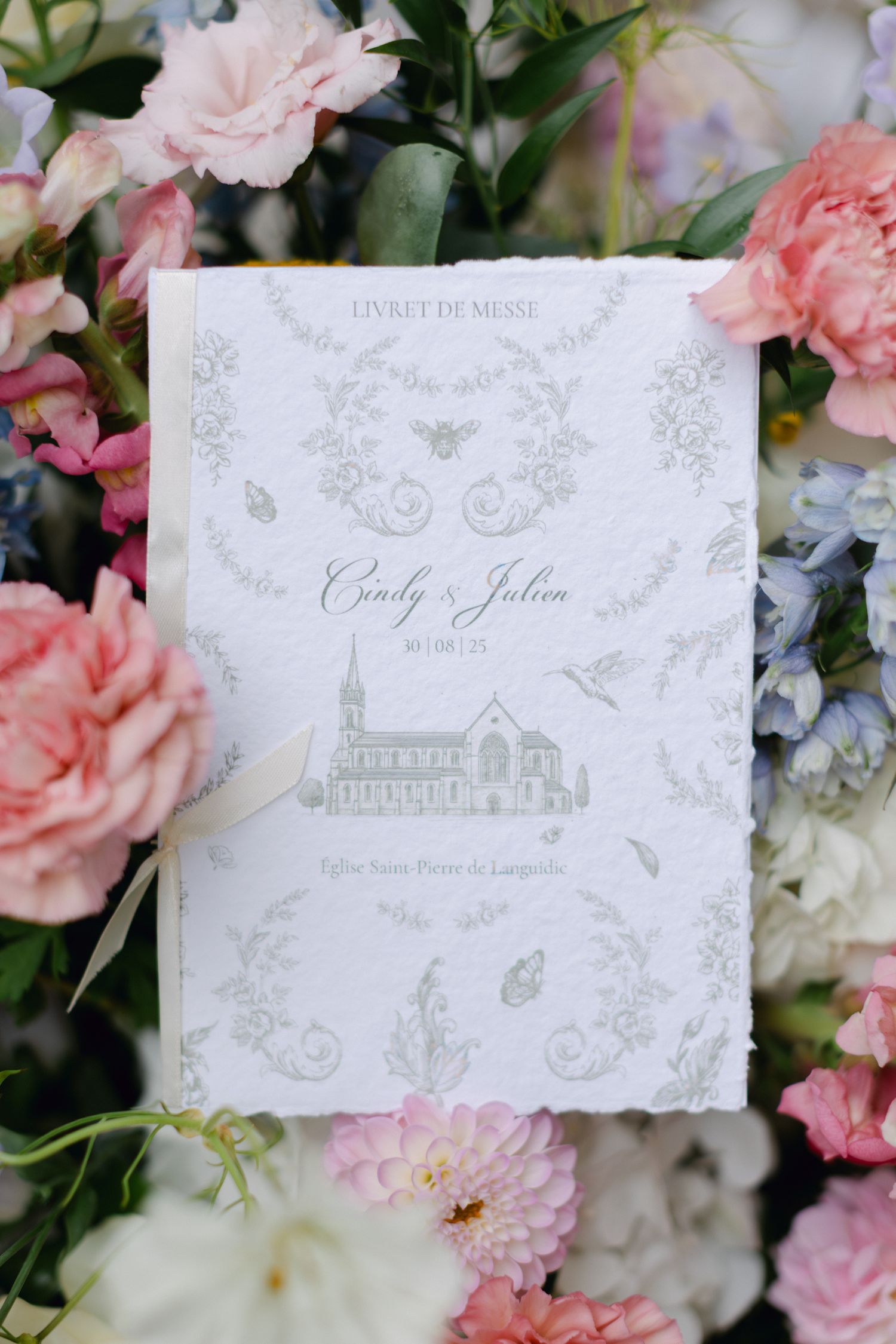Livret de cérémonie de mariage élégant pour Cindy et Julien entouré de fleurs roses et bleues douces.