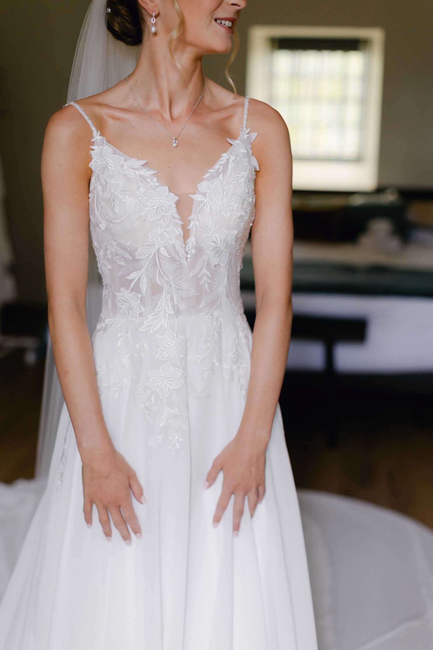 Mariée en élégante robe de mariée en dentelle A-line avec voile et collier délicat posant à l'intérieur.
