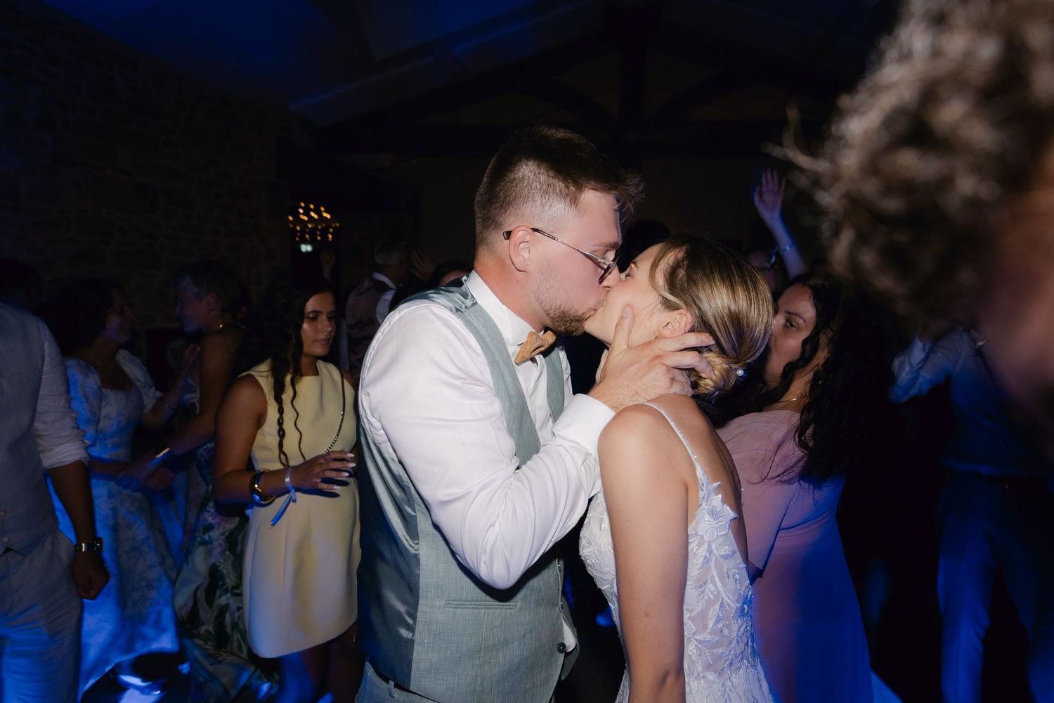 Les jeunes mariés partagent un baiser passionné sur la piste de danse entourés d'invités à la réception de mariage.